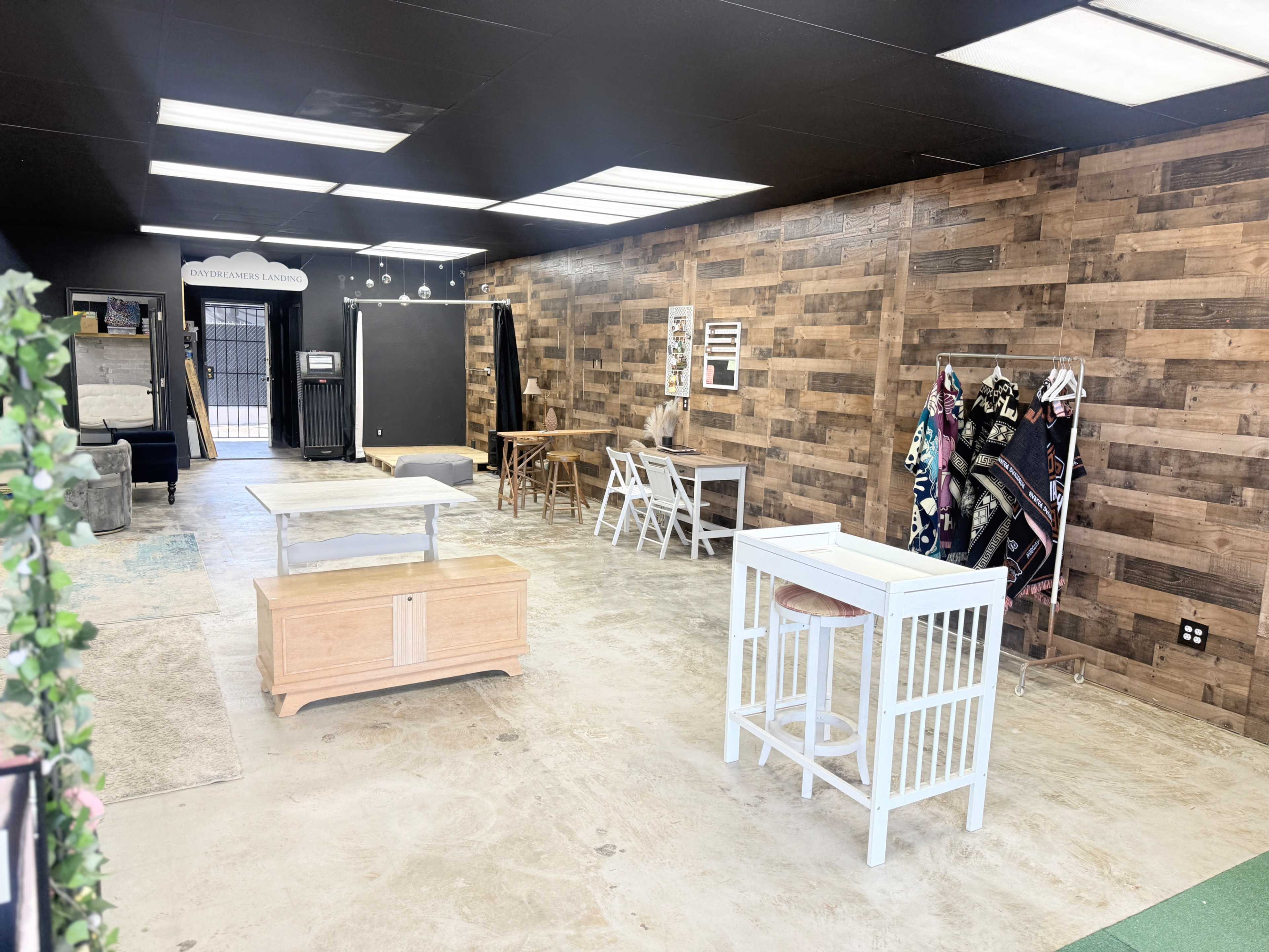 The image shows a spacious, empty room with a wood-paneled wall, various tables, and chairs arranged throughout the area.