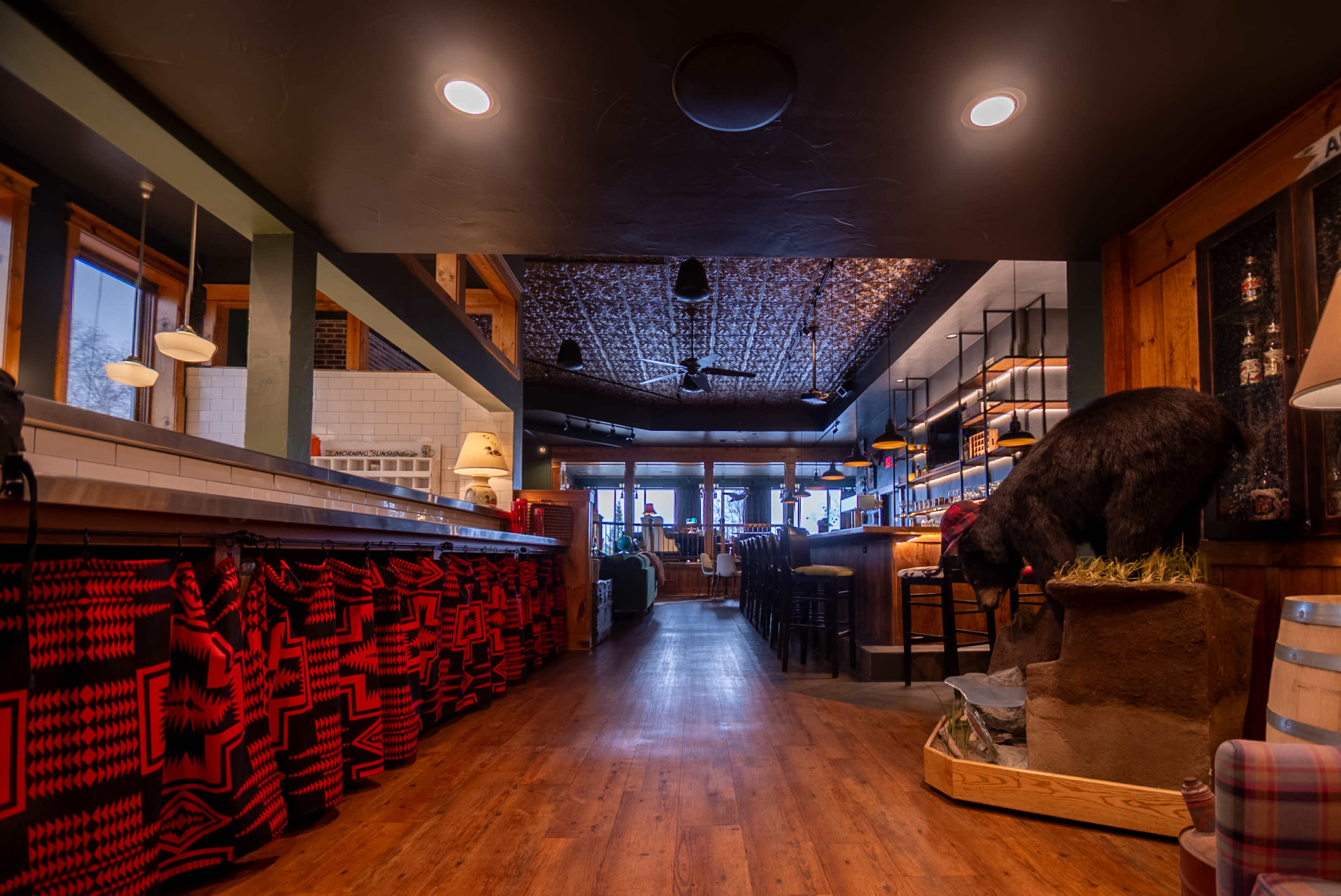 The image shows the interior of a restaurant with wooden flooring, a bar area on the left, and a bear sculpture positioned on a grassy base near the entrance.