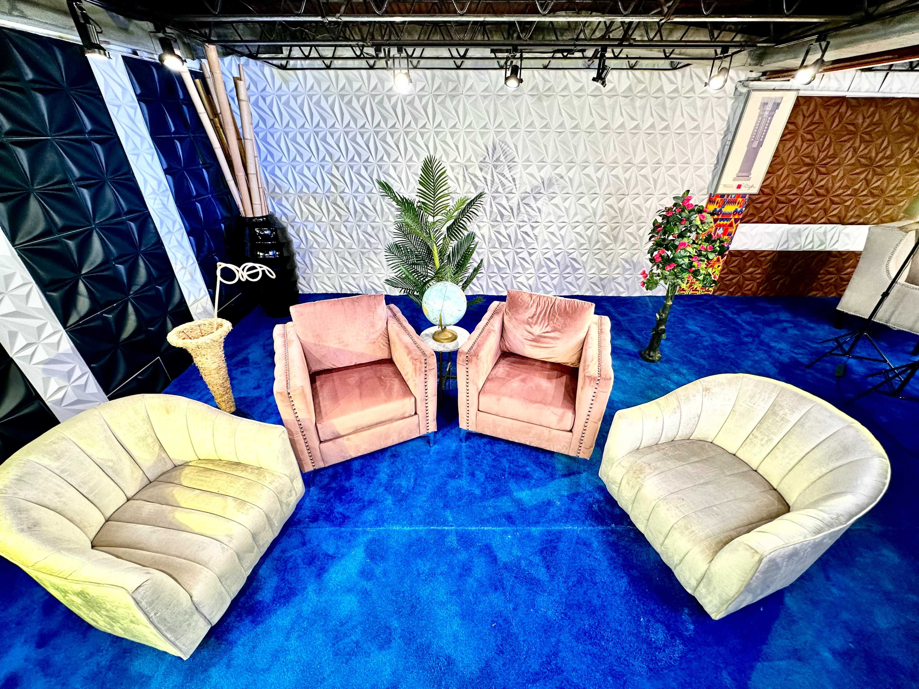 A brightly lit room with four upholstered chairs arranged around a small globe and a potted plant on a blue carpet.