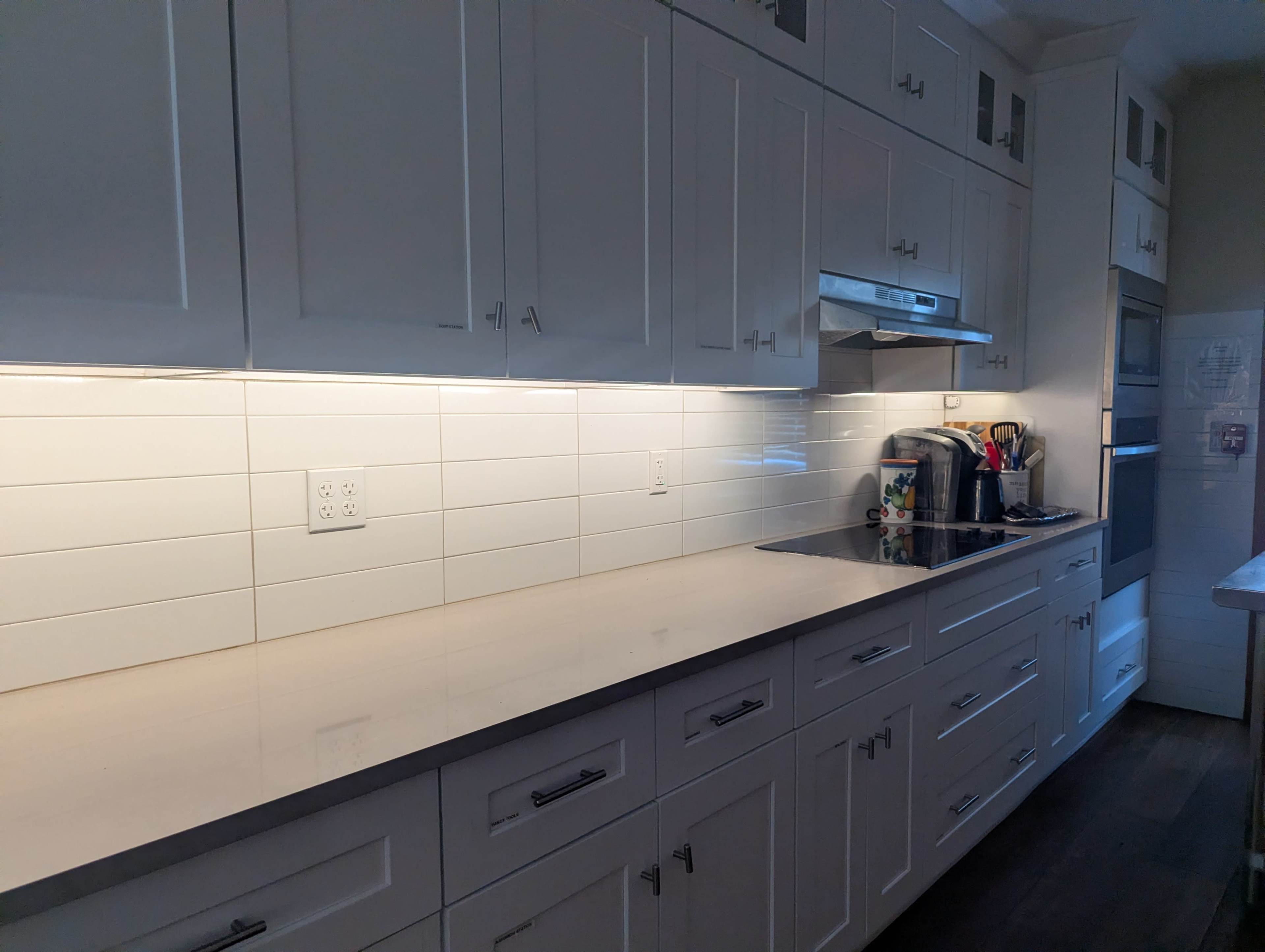 The image shows a modern kitchen with white cabinetry, a gray countertop, and a stainless steel kitchen appliance setup against a white subway tile backsplash.