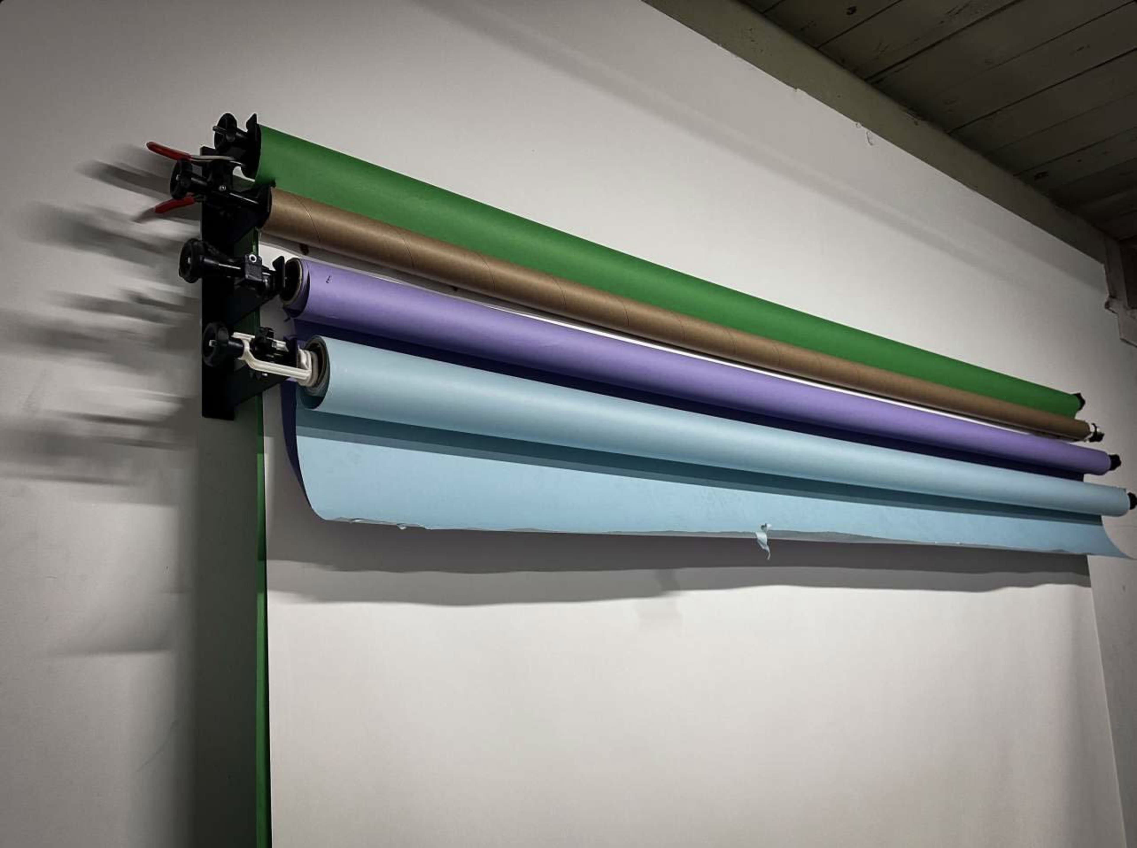 A wall-mounted background system displays several rolls of colored paper in green, brown, lavender, and blue.