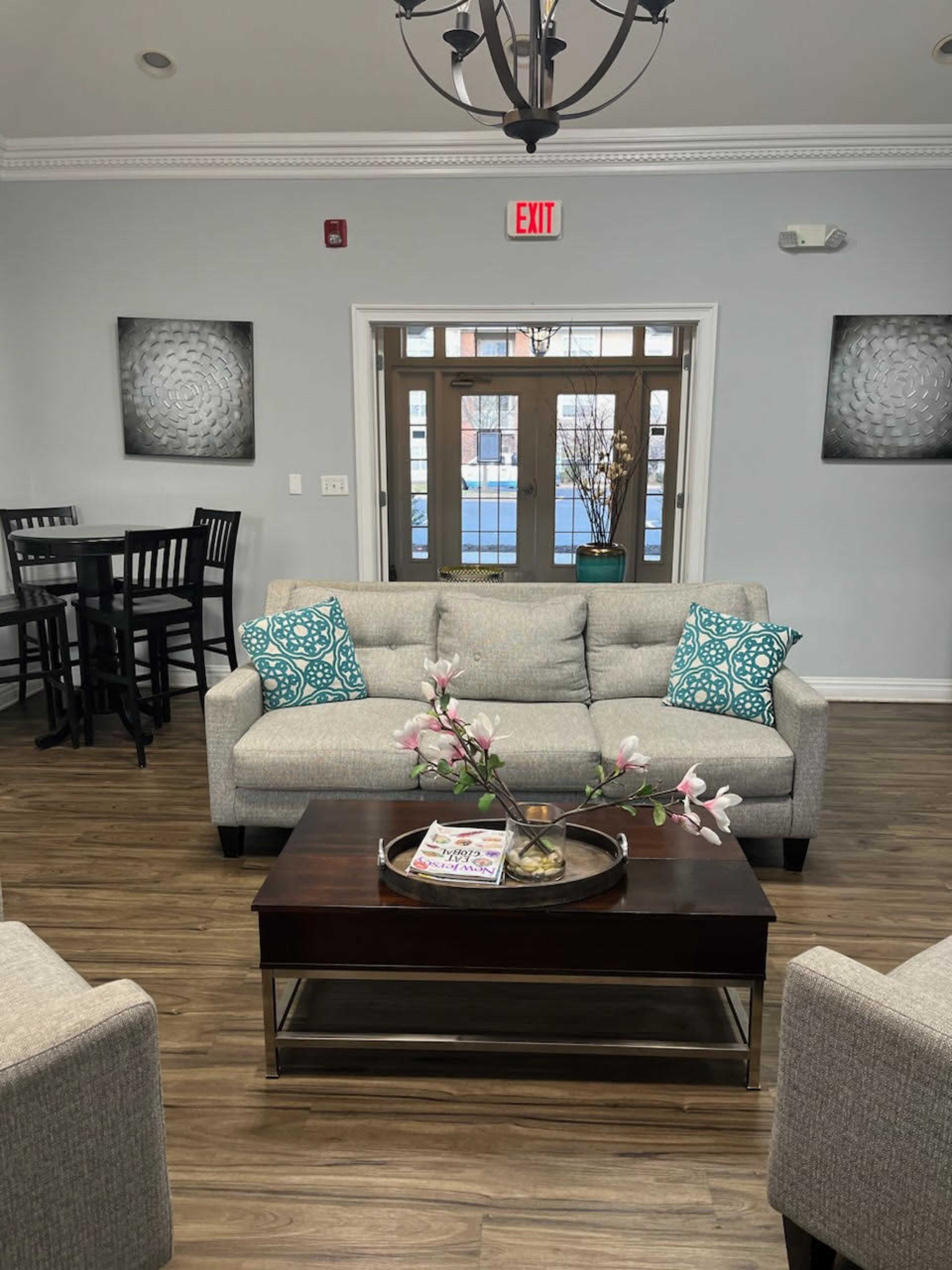 A bright, modern lounge area features a gray couch with turquoise pillows, a wooden coffee table with a decorative tray, and two matching armchairs.