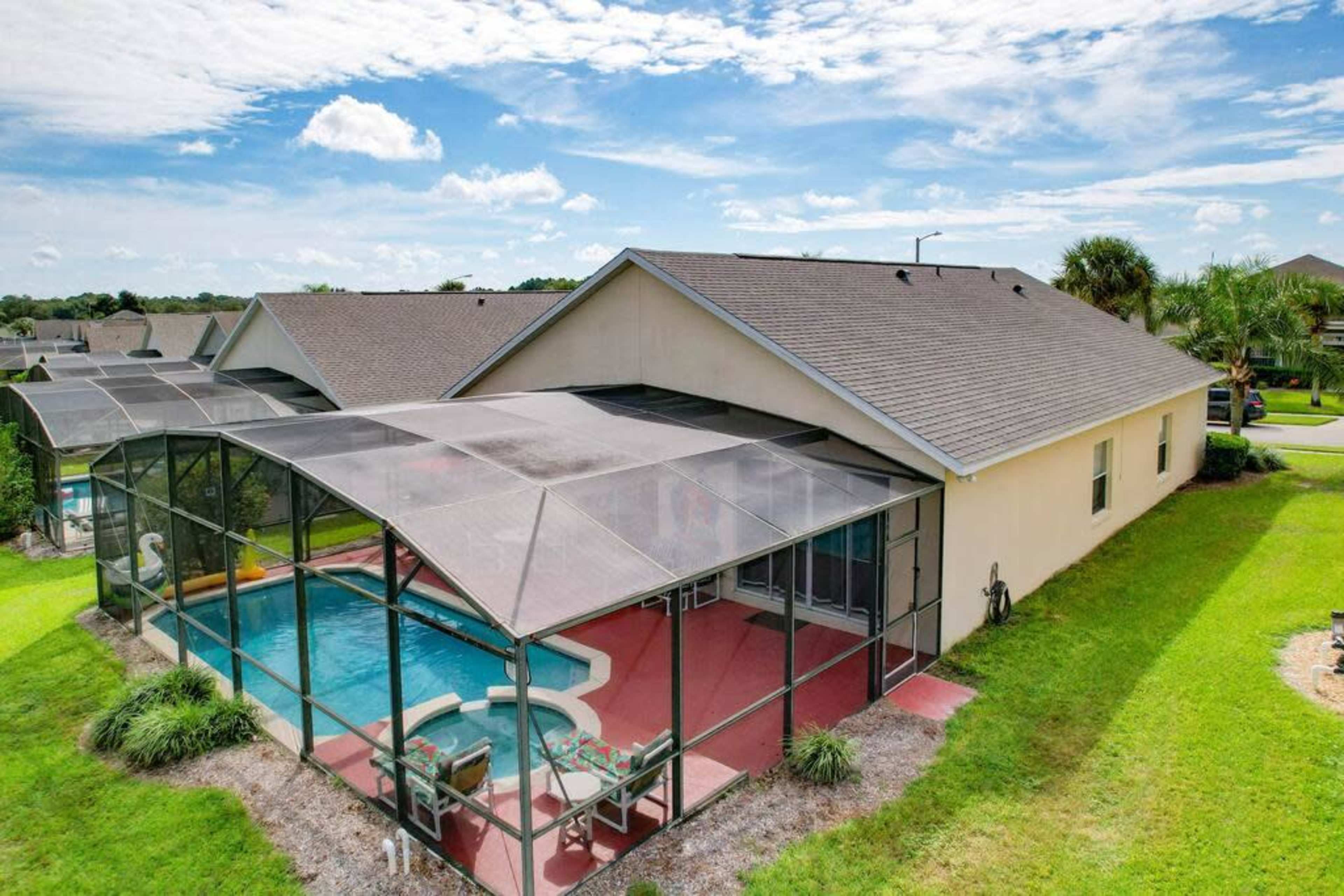 The image shows a single-story house with a screened-in patio covering a pool, surrounded by a grassy yard and residential neighbors in the background.