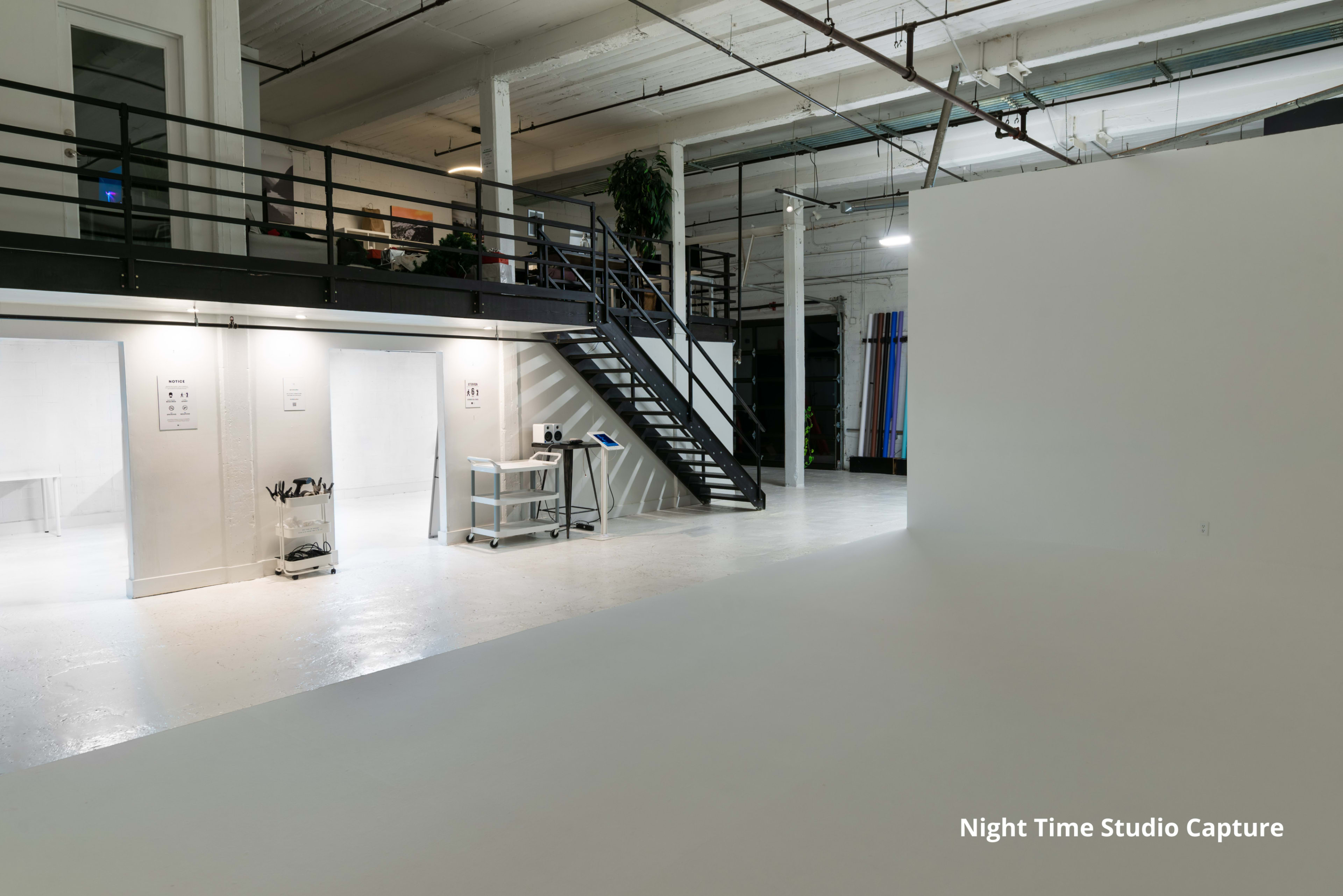 A spacious, well-lit studio with a staircase leading to an upper level and various workspaces along the walls.