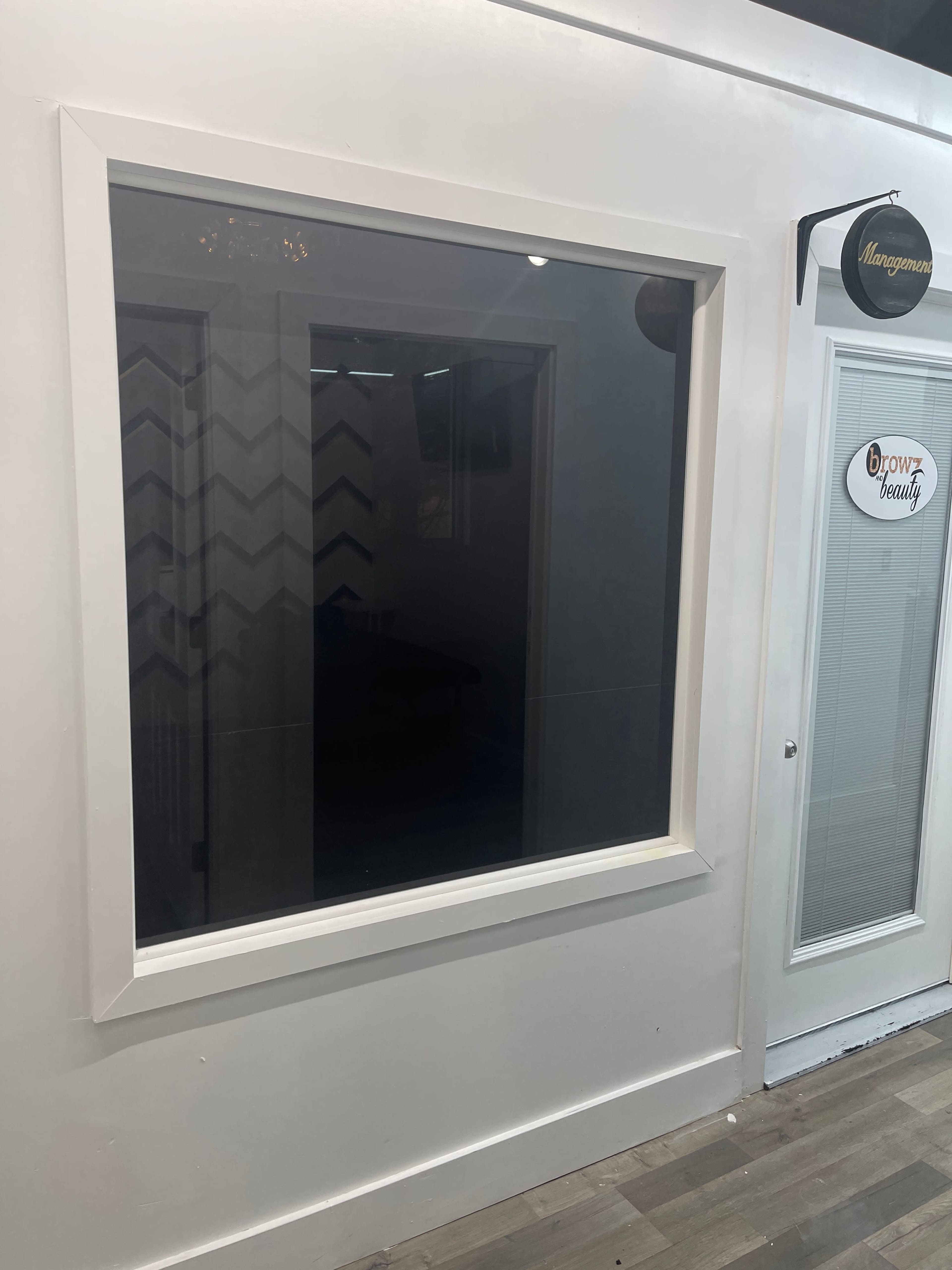 A large, blank window with a white frame is mounted on a wall next to a door labeled "Management."