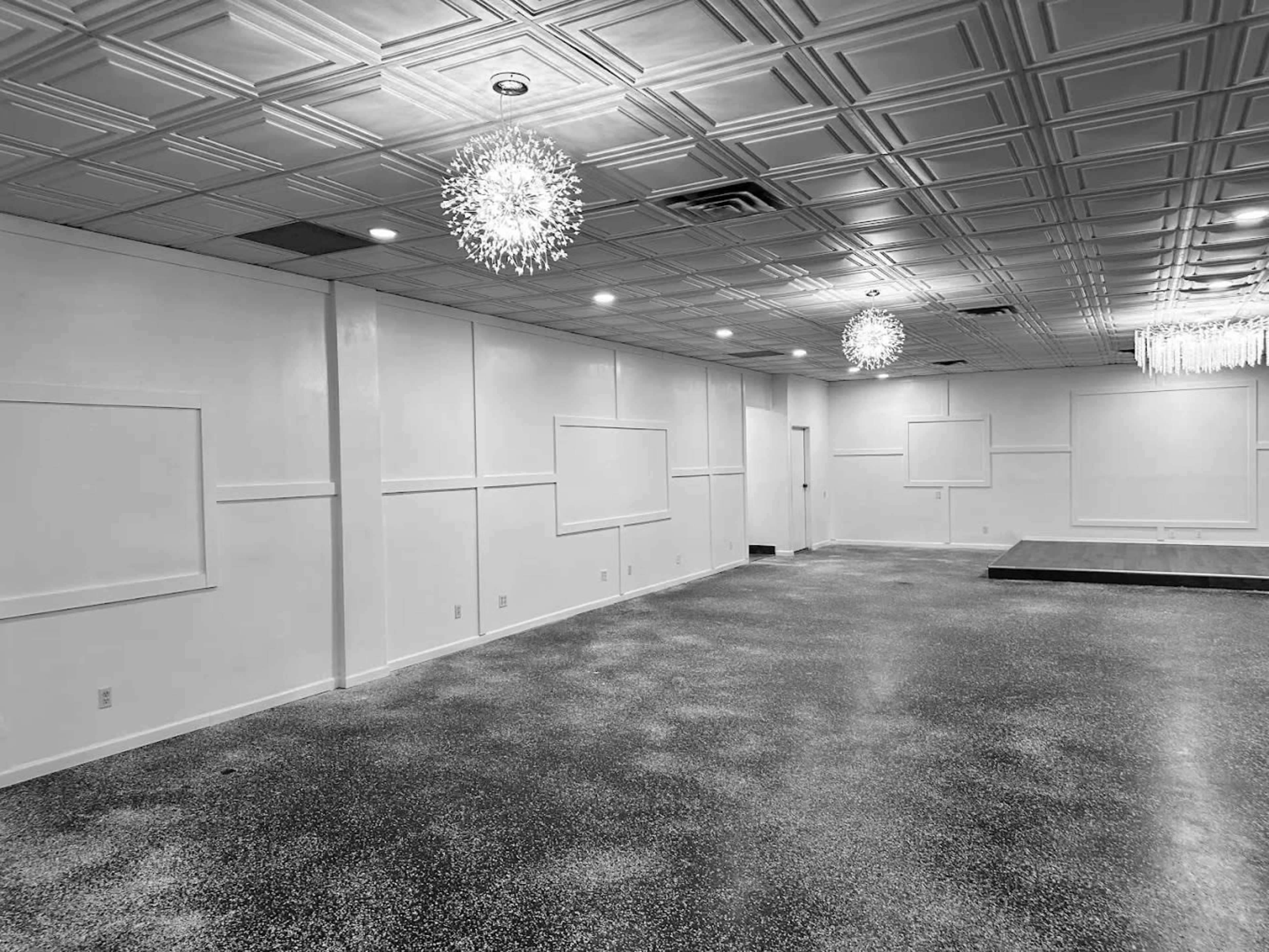 The image shows a spacious room with a textured ceiling, two decorative light fixtures, and a stage area at one end.