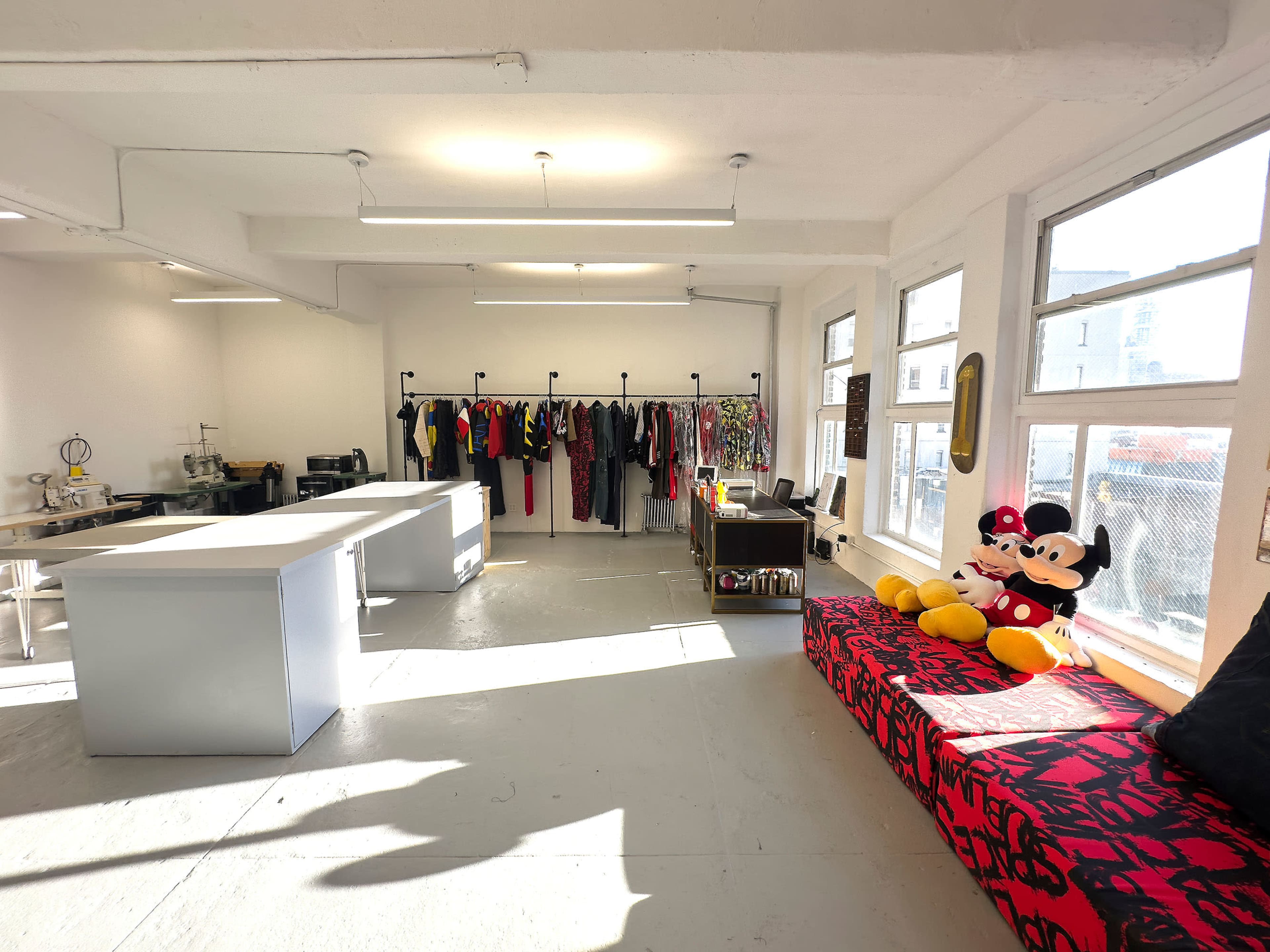 The bright, spacious room features a clothing rack filled with garments, a large table, and a colorful seating area with plush toys.
