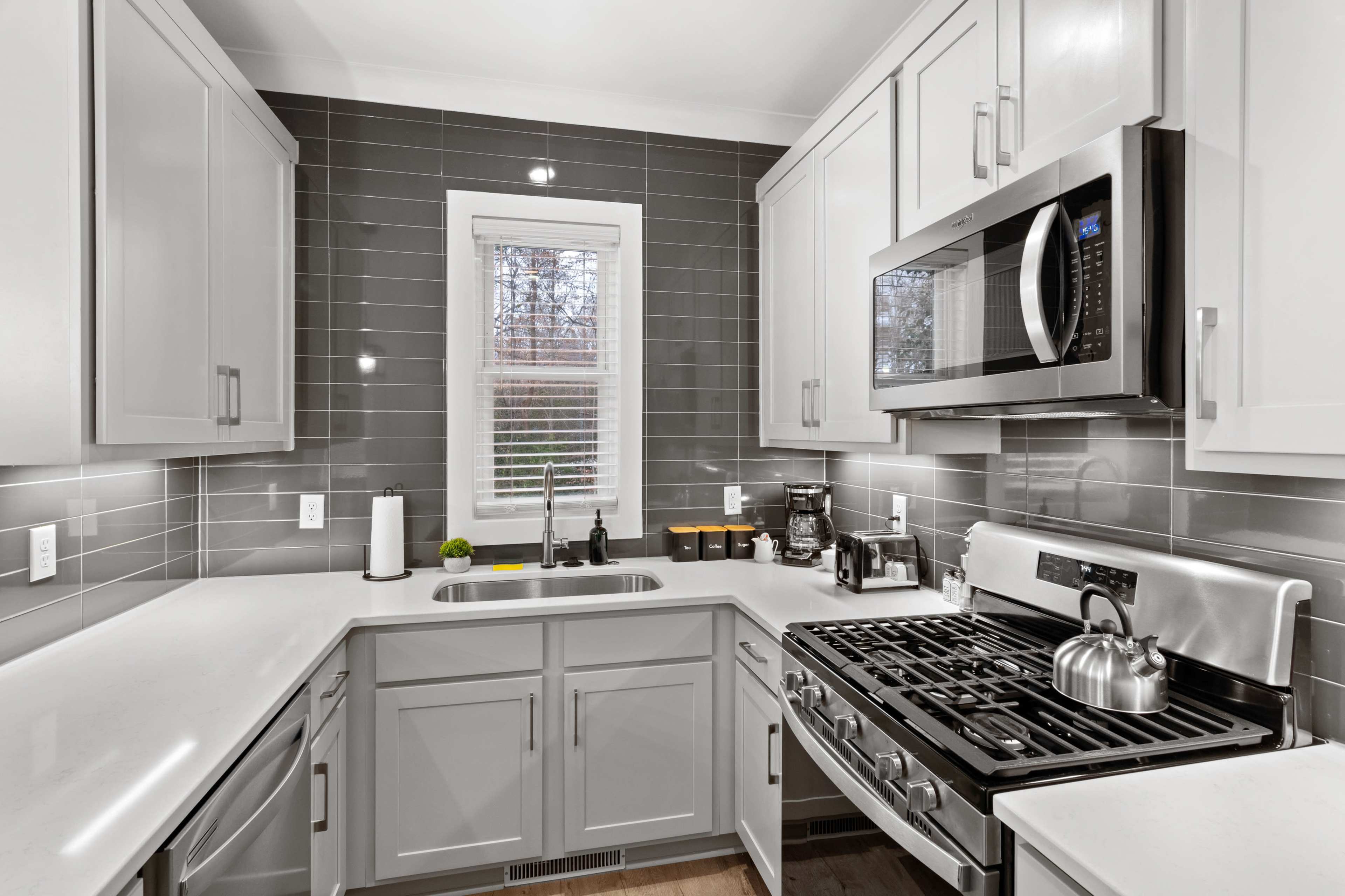 A modern kitchen with gray cabinets, stainless steel appliances, a gas stove, and a window letting in natural light.