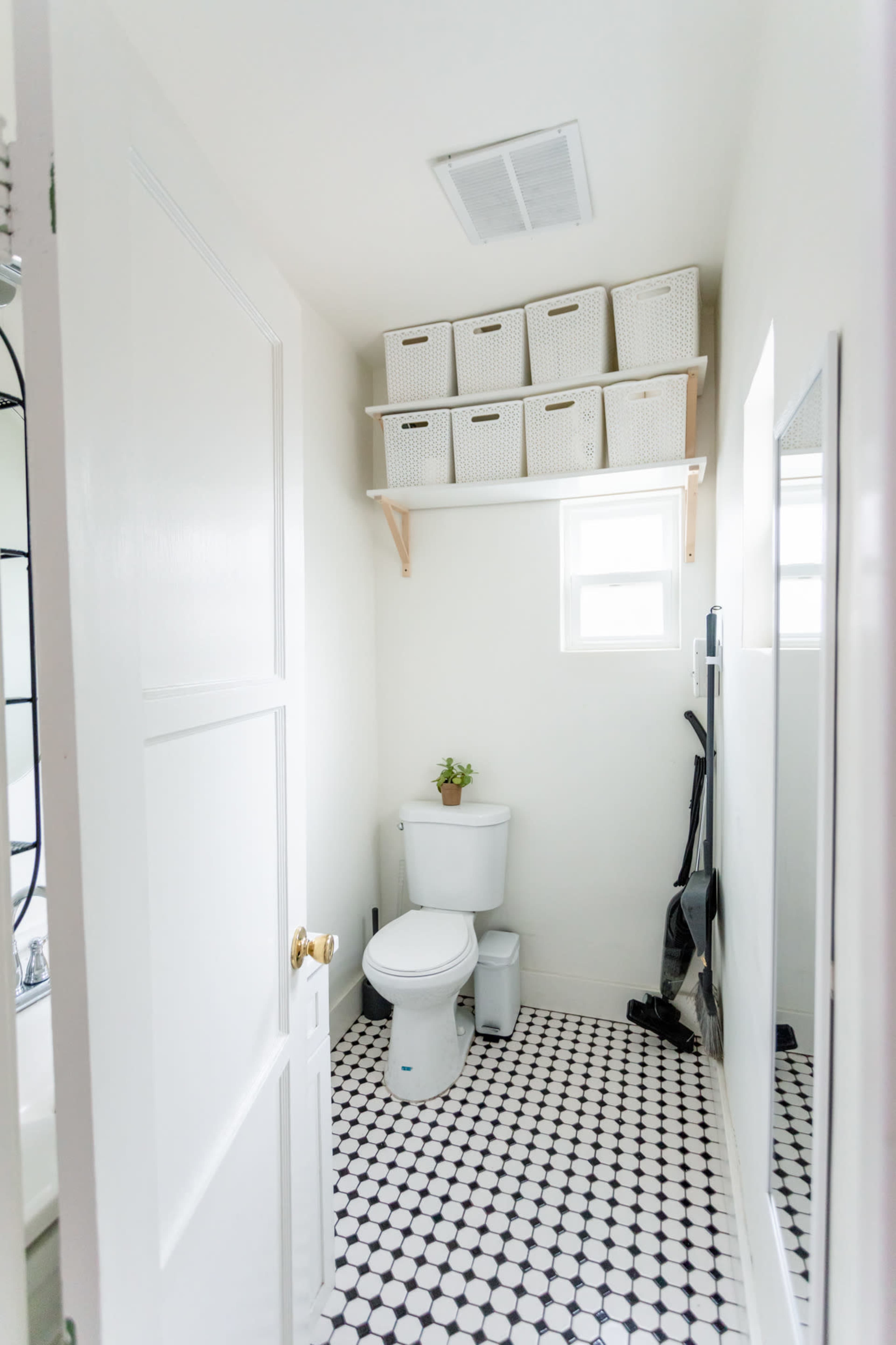 A small bathroom features a toilet next to a window, with shelves above storing woven baskets.