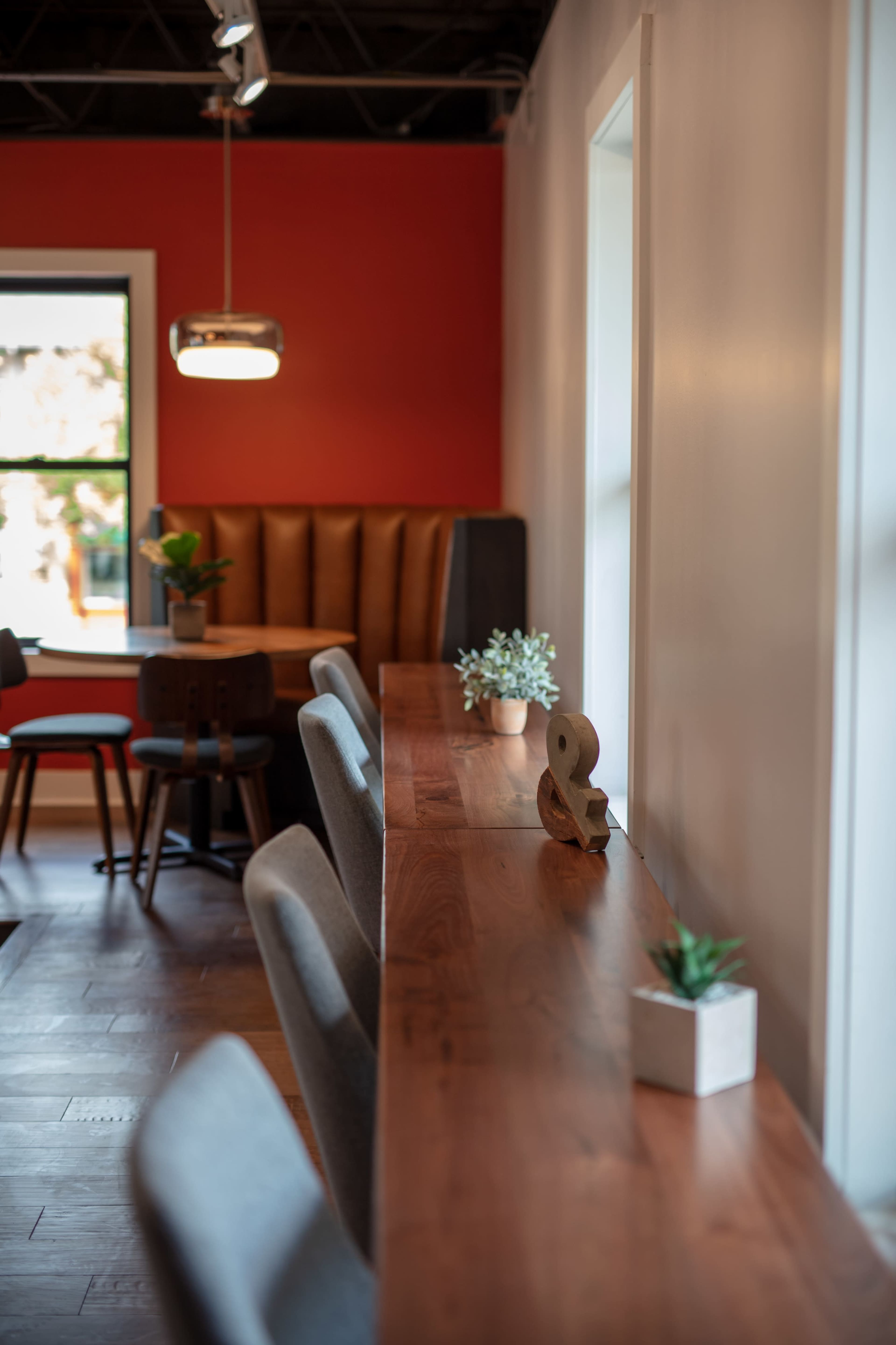 The image shows a modern interior of a café or workspace with a long wooden table, seating, and decorative plants along the tabletop.