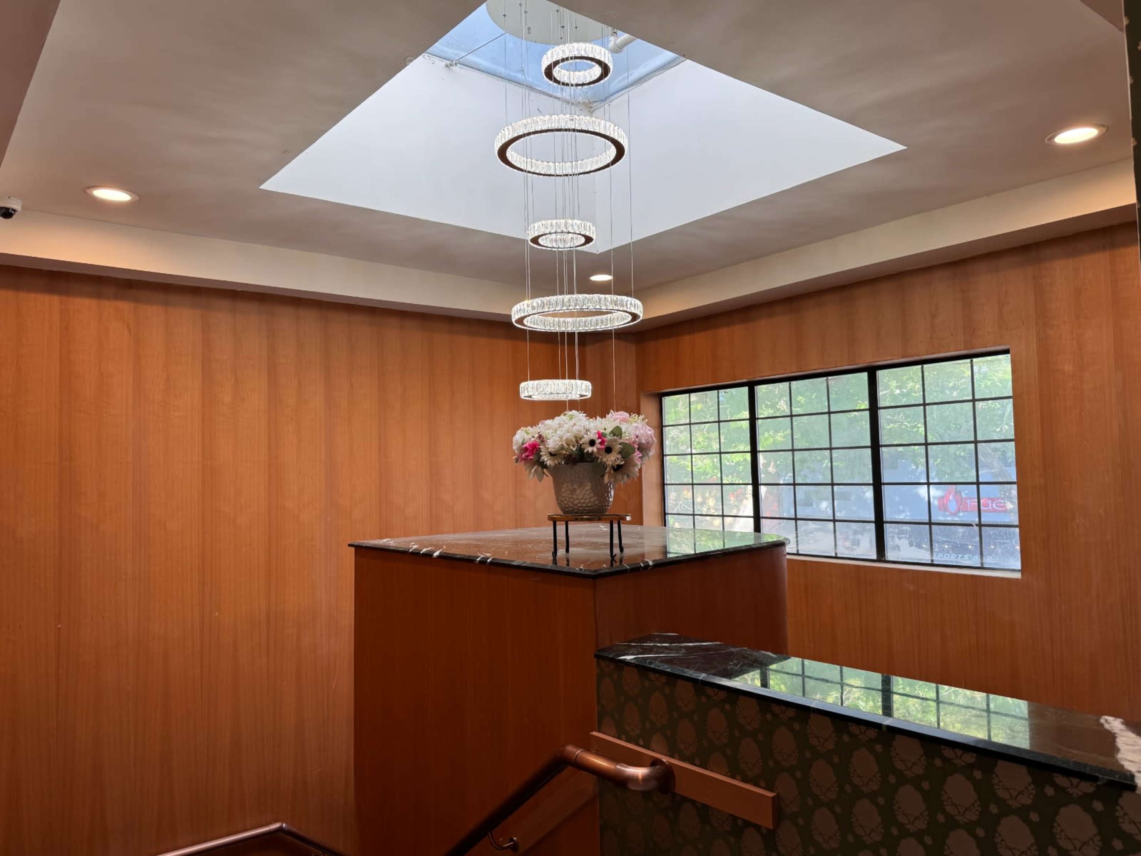 The image shows a staircase leading up to a landing with a decorative arrangement of flowers inside a vase, beneath a skylight and surrounded by wooden walls.
