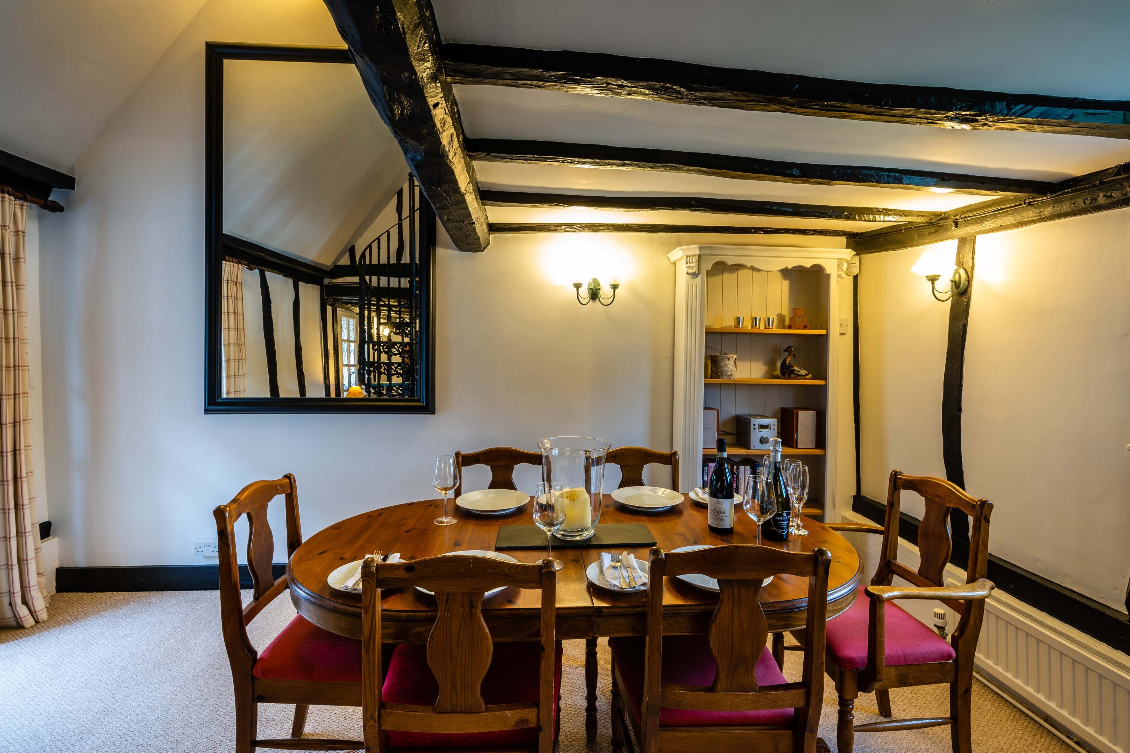 A wooden dining table is set with plates and glasses in a room featuring exposed beams and a large mirror on the wall.