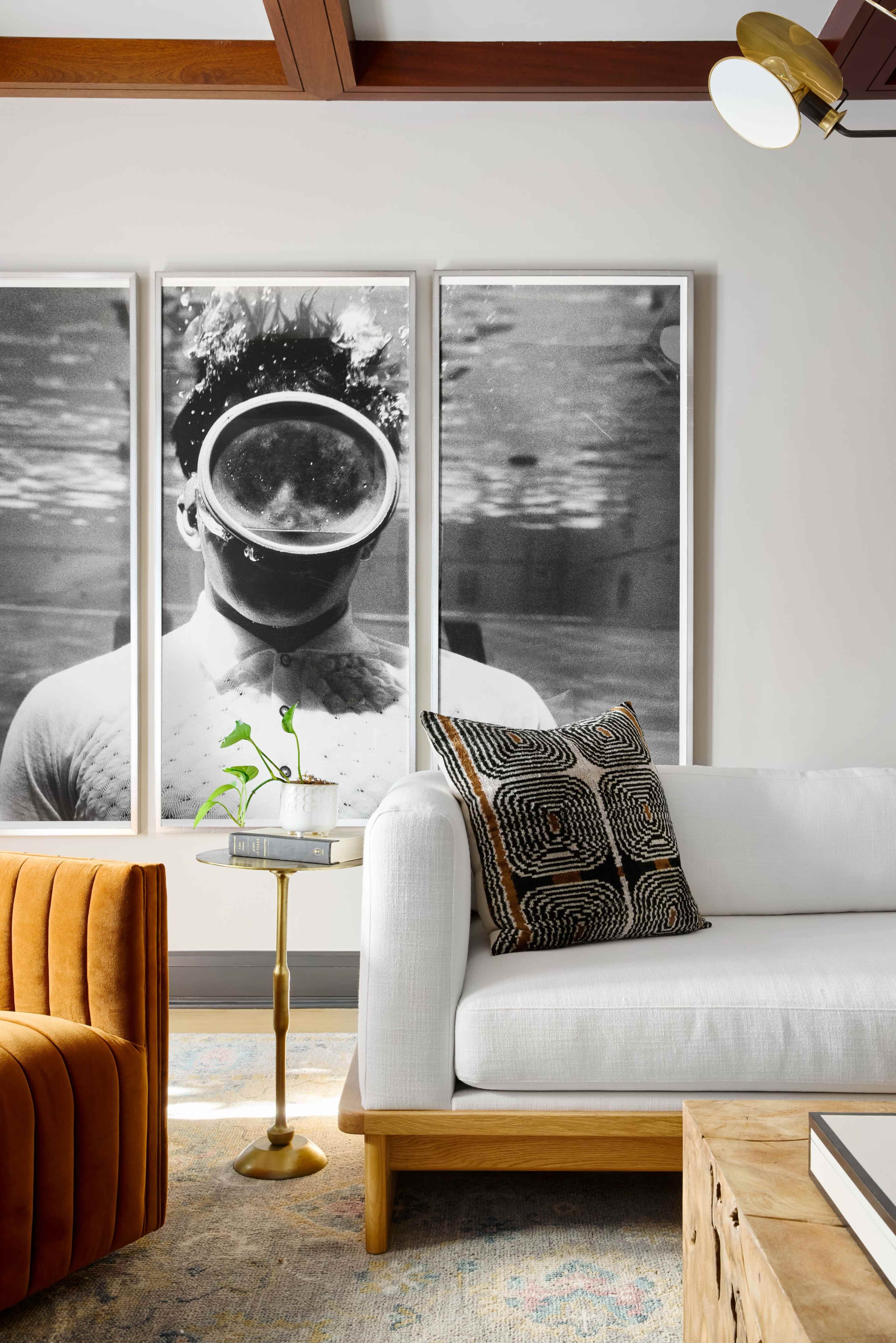 A modern living room with a white sofa, an orange armchair, a round side table, and three large black-and-white photographs on the wall.