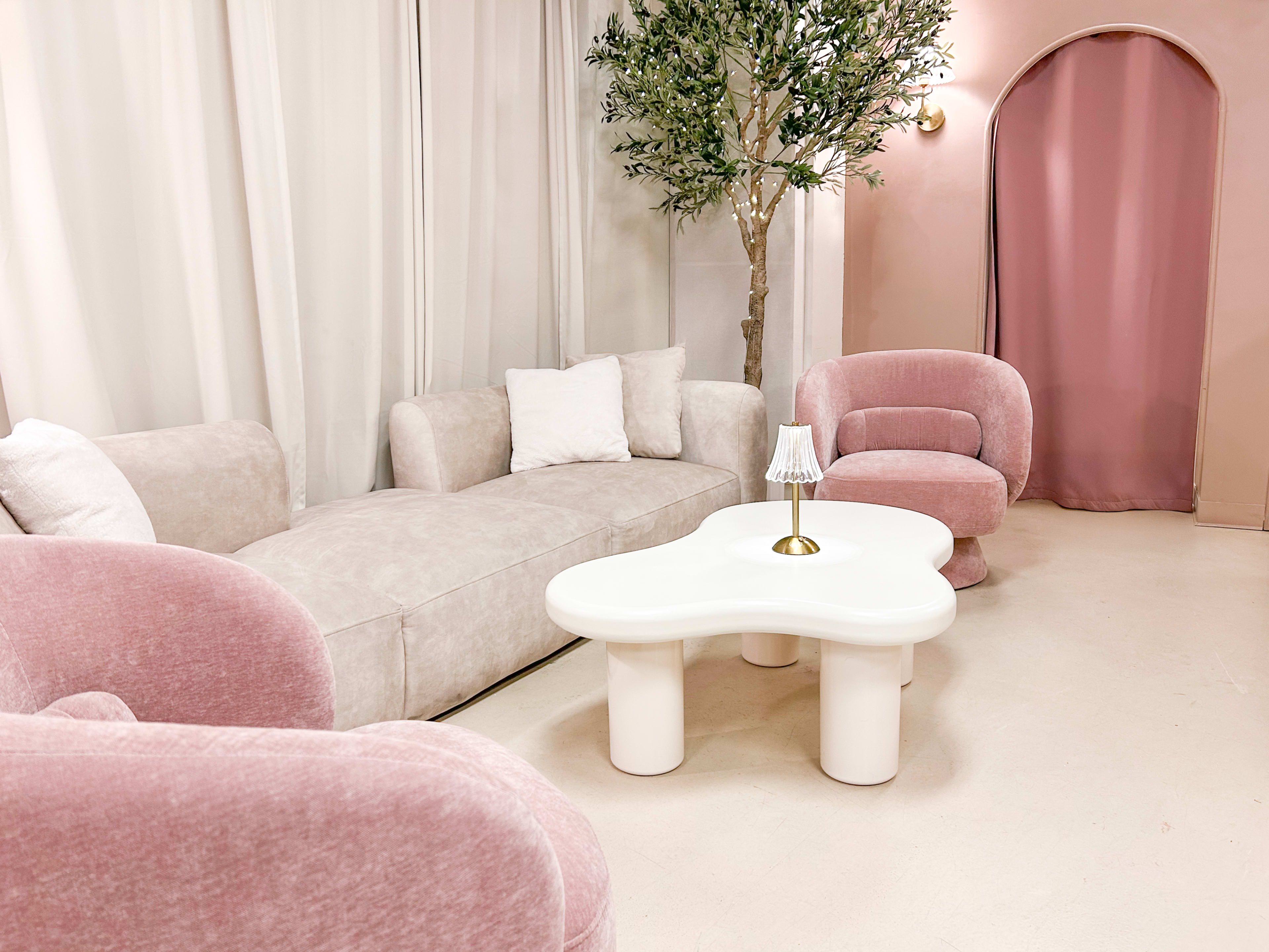 The image shows a cozy living room with a light pink sofa, two round armchairs, and a whimsical white coffee table under soft lighting.