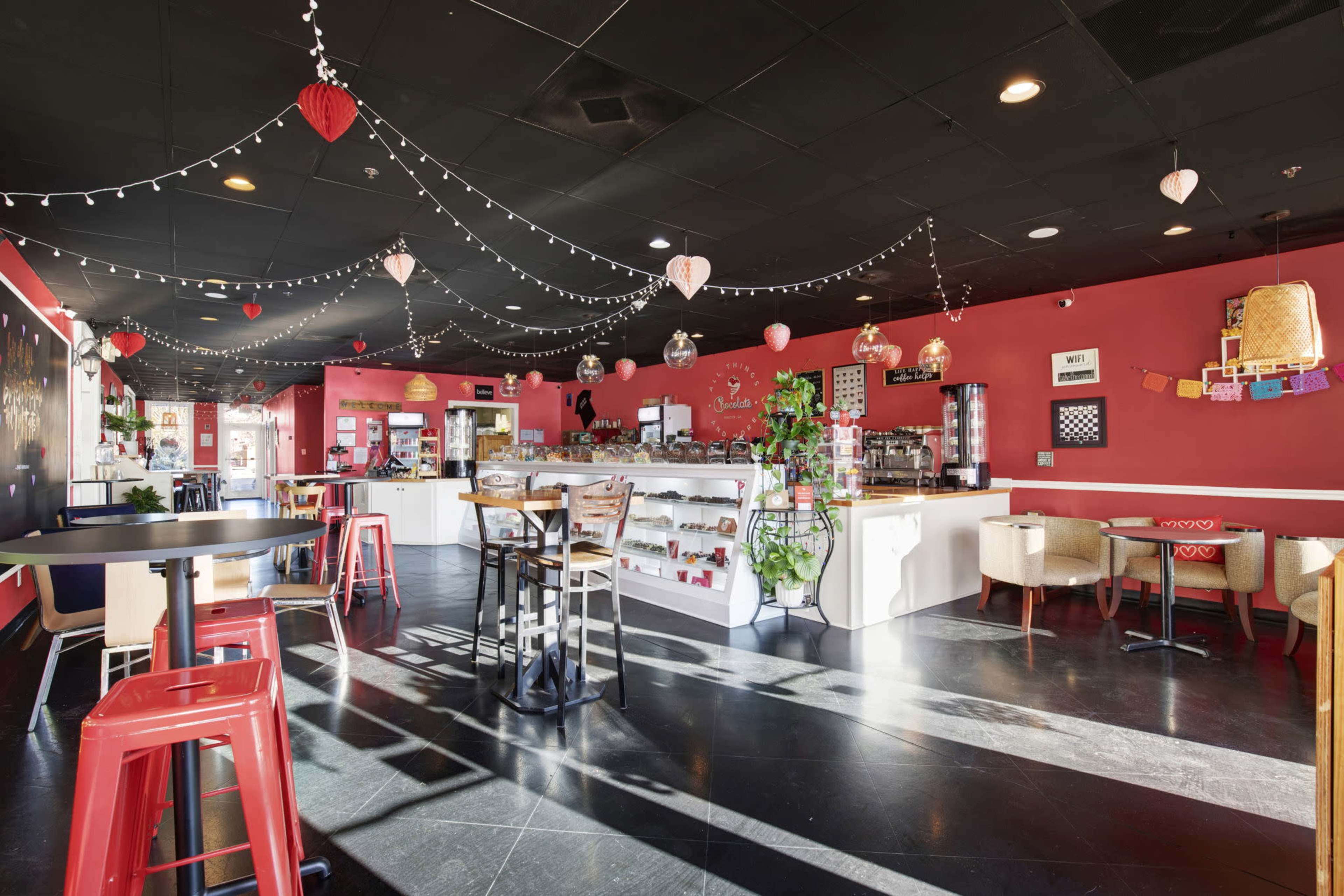 The image shows a brightly colored café interior with red walls, various seating options, and decorative hanging lights.