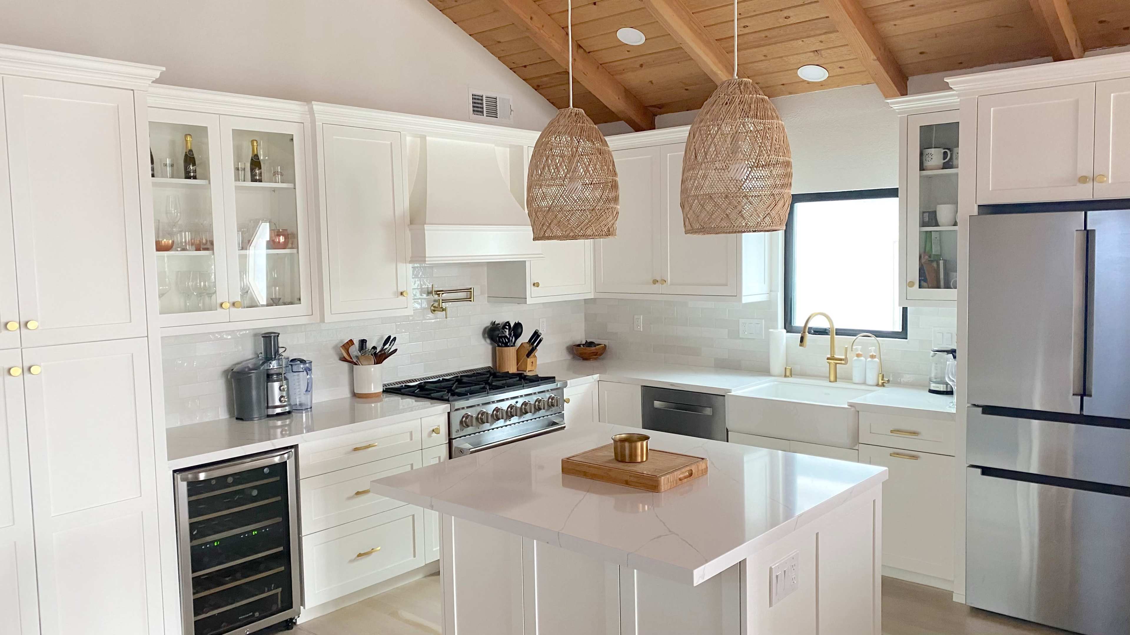 The kitchen features white cabinetry, a large island with a wooden tray, and pendant lights hanging above, complementing stainless steel appliances.