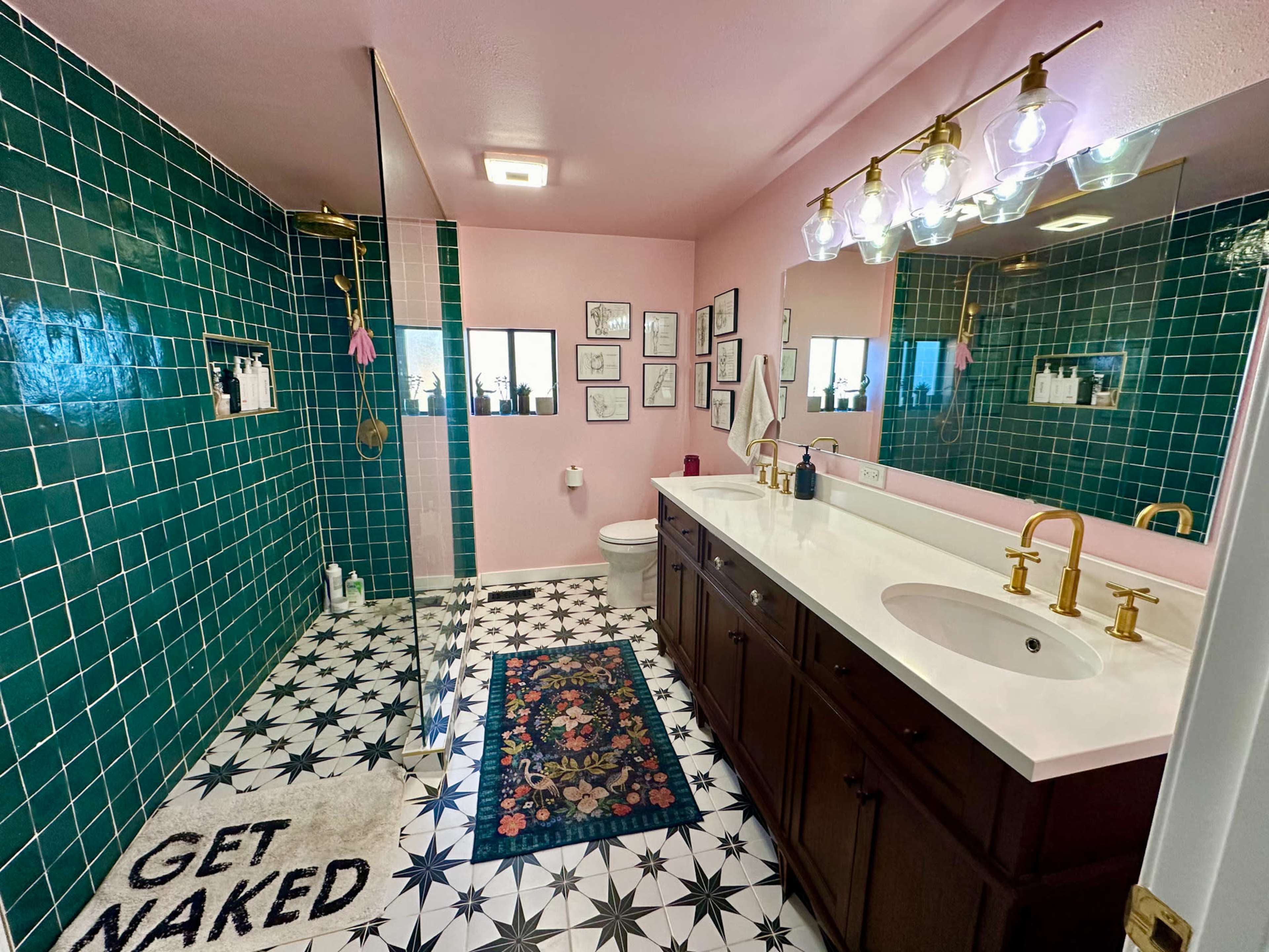 The bathroom features green tiled walls, a glass-enclosed shower, a double vanity with gold fixtures, and decorative tile flooring.
