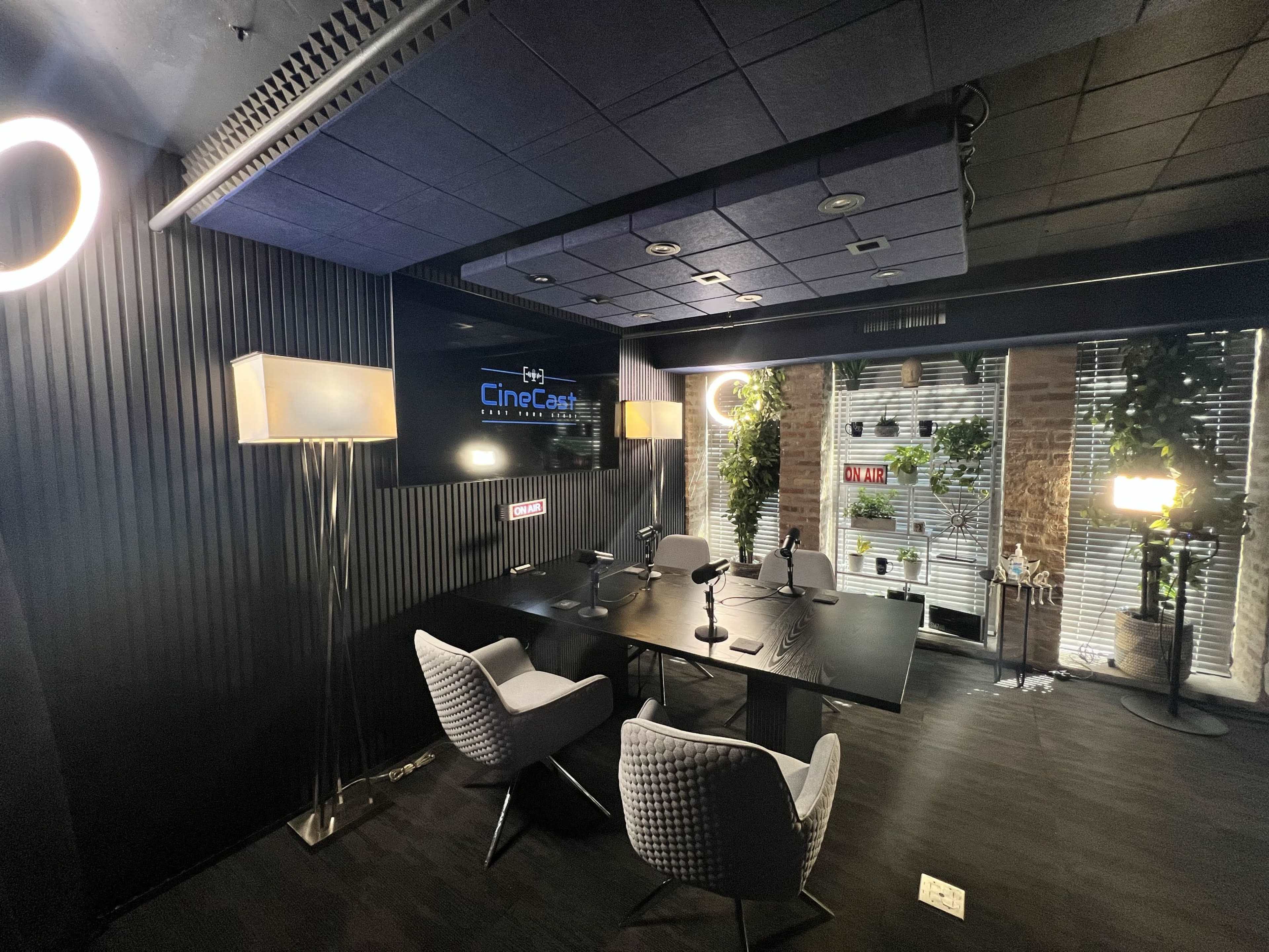 The image shows a modern meeting room with a large table, four chairs, and various lighting fixtures, along with a screen displaying a logo.