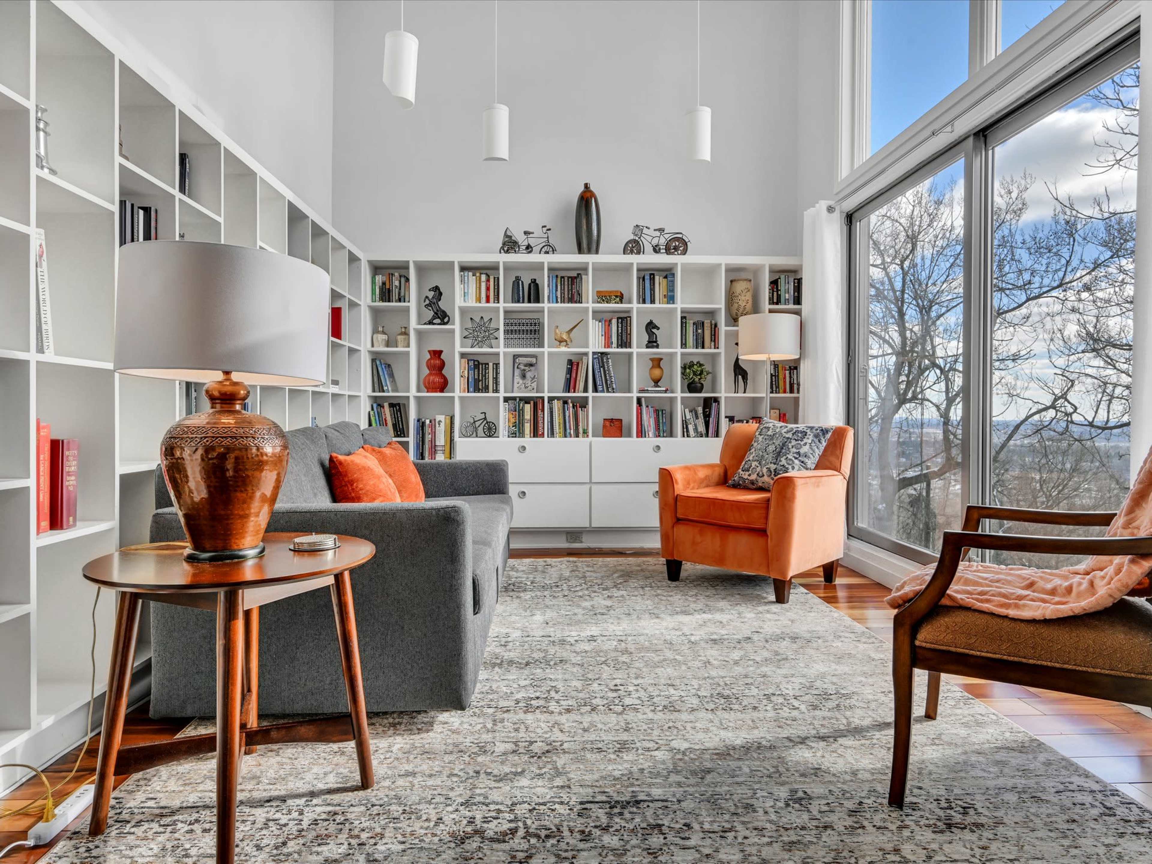 A modern living room featuring a gray sofa, an orange armchair, a round wooden side table, and a bookshelf filled with various books and decorative items.