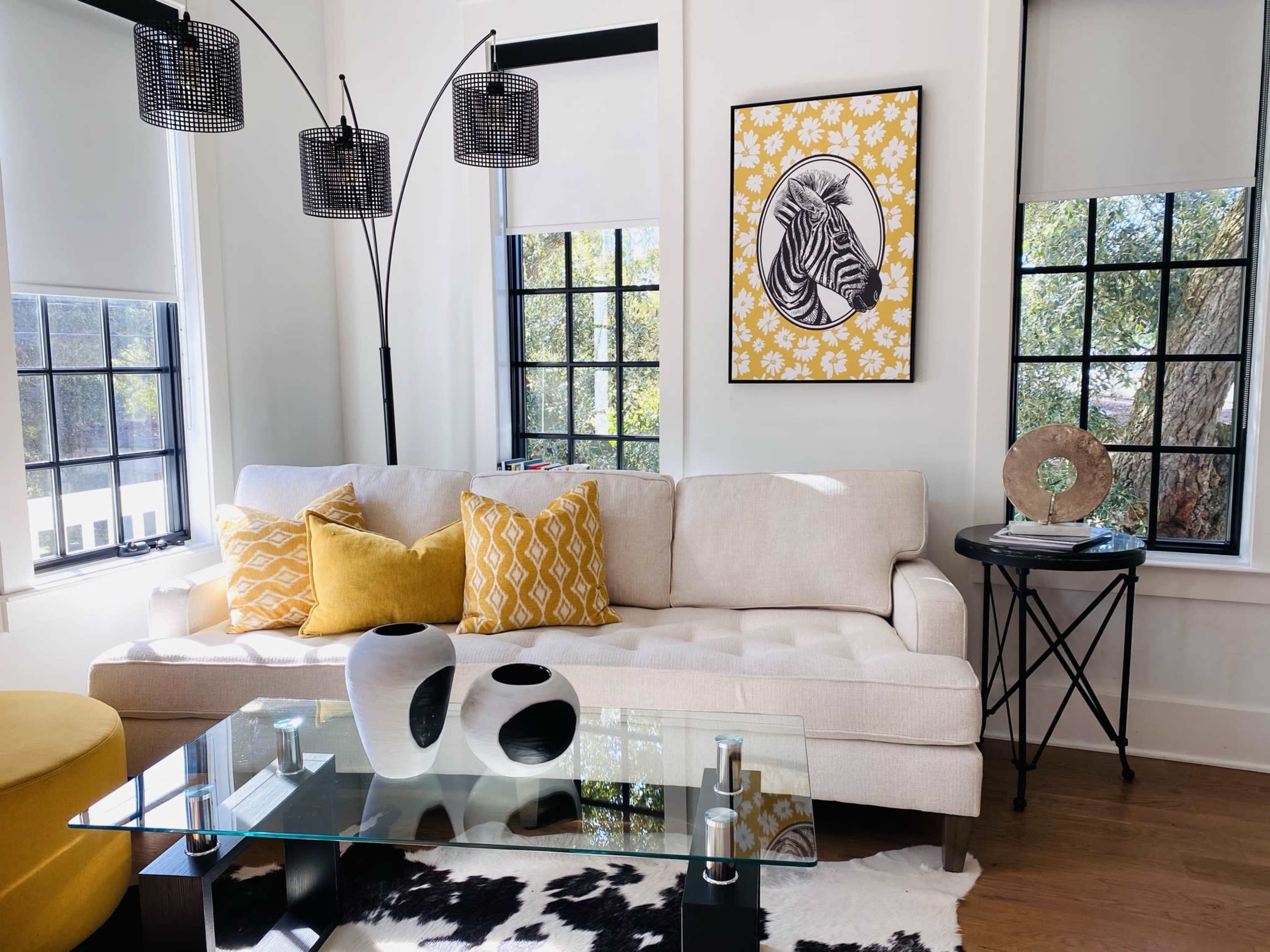 A modern living room featuring a beige sofa with yellow patterned pillows, a glass coffee table, and a zebra print artwork on the wall.