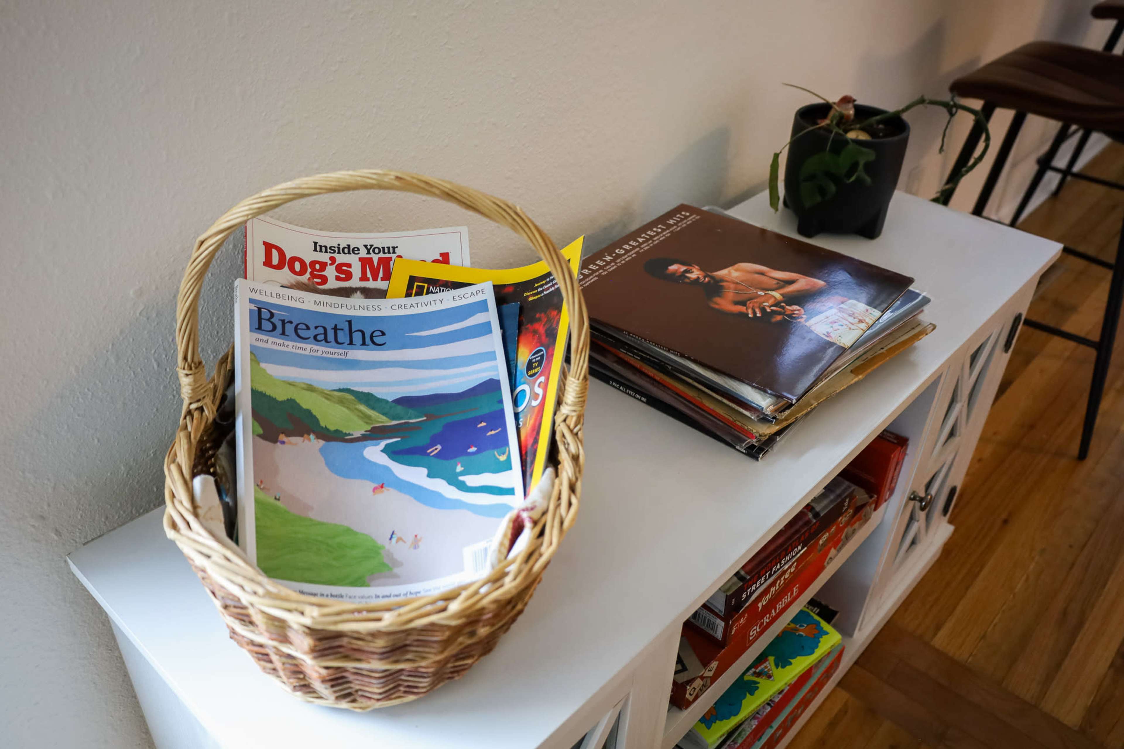A woven basket filled with magazines sits on a white shelf alongside a stack of vinyl records and a small plant.