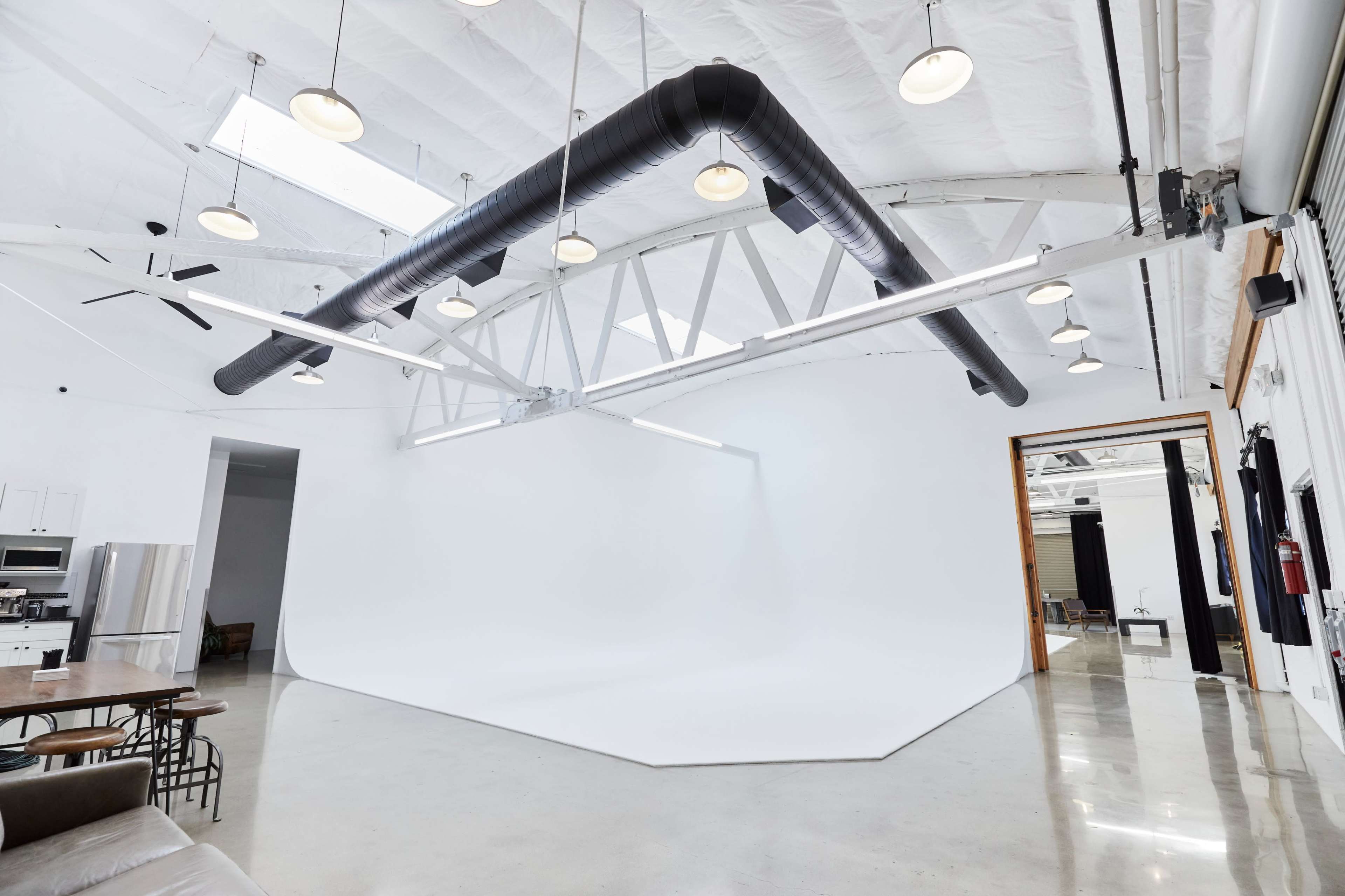 The image shows a spacious, well-lit studio with a white backdrop and industrial-style lighting and ventilation.