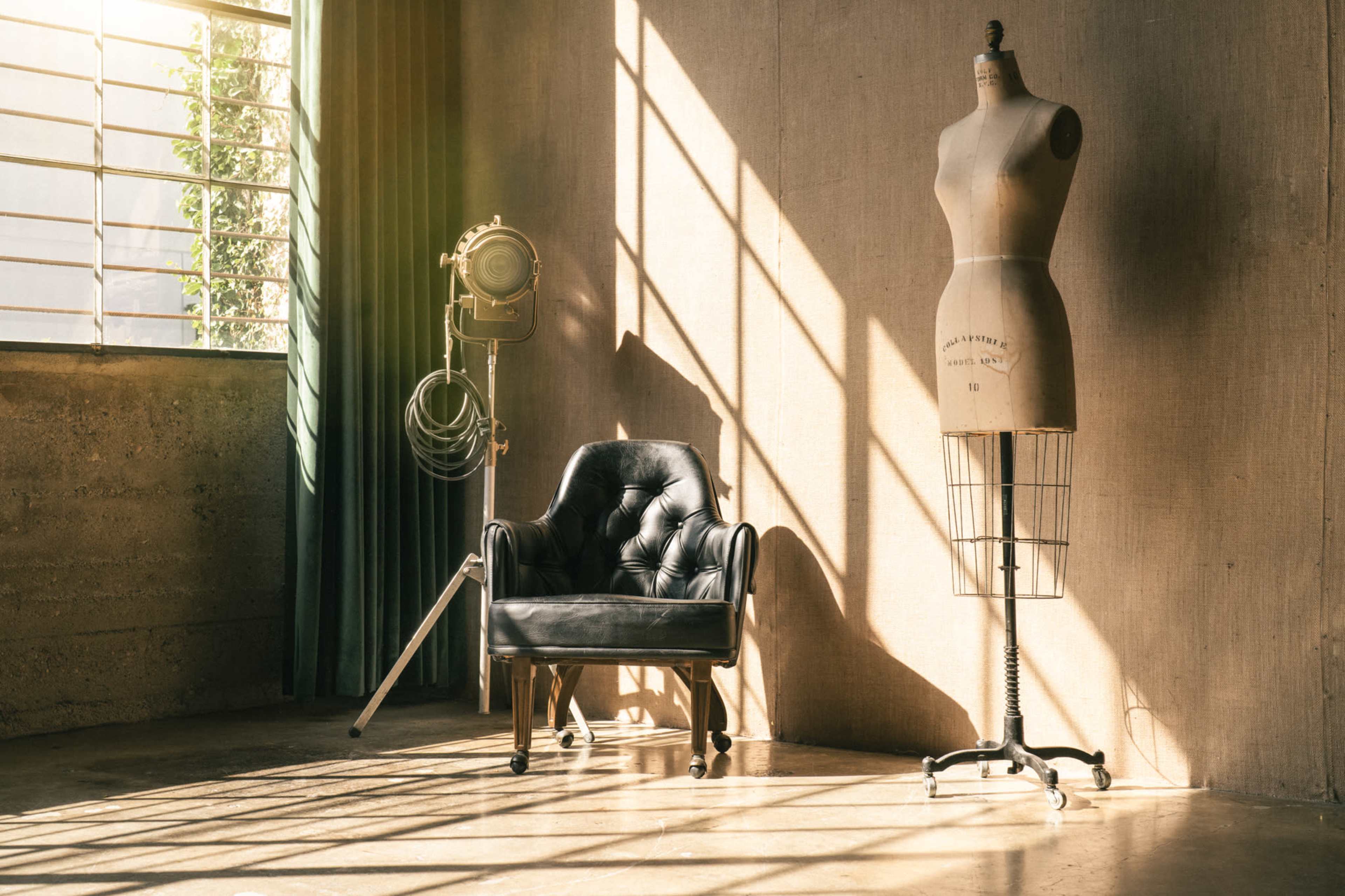 A black upholstered chair and a dress form standing beside a large window with sunlight creating patterns on the floor.