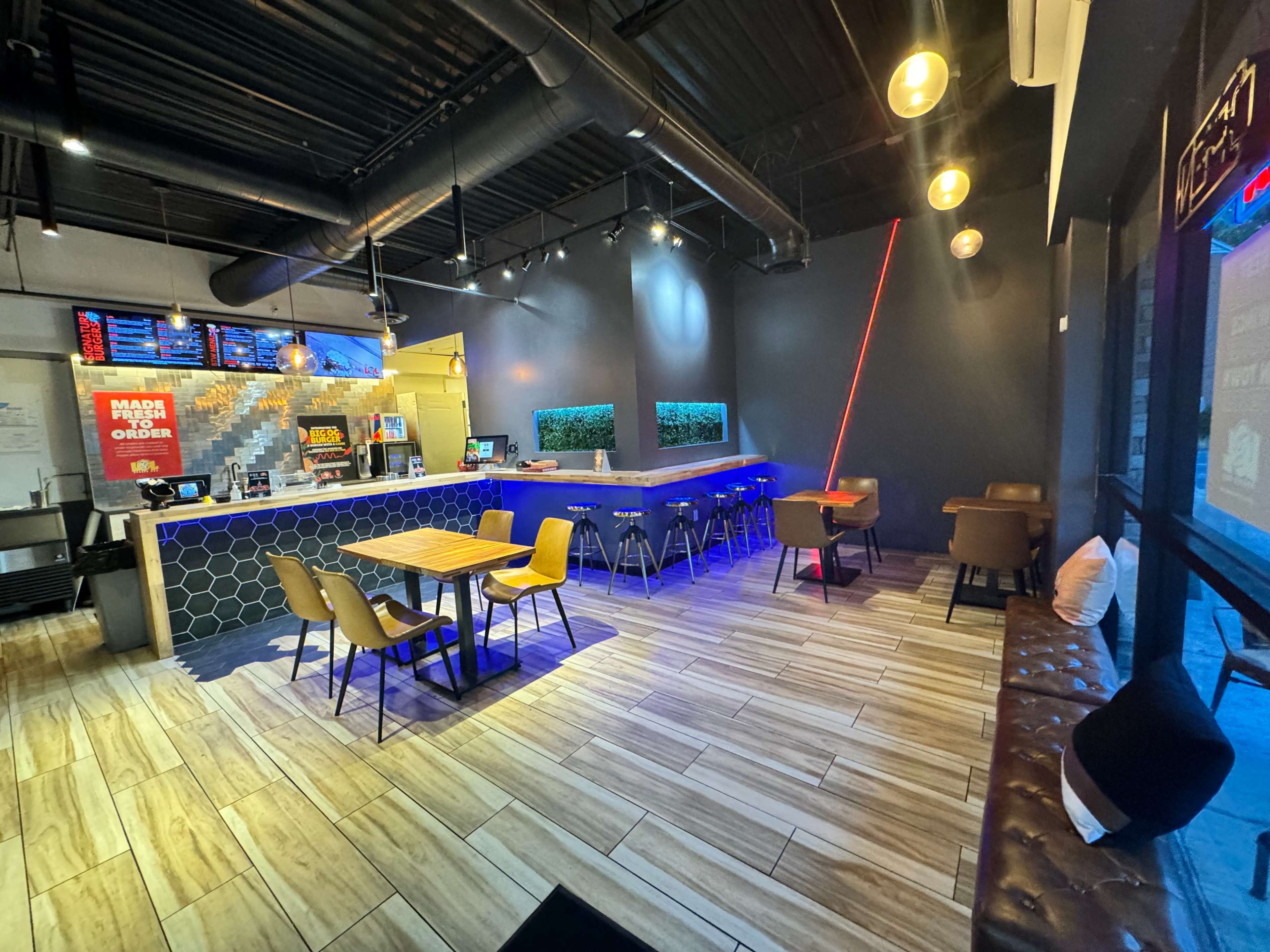 A modern restaurant interior featuring a bar area, wooden tables, and a seating space with a leather bench.