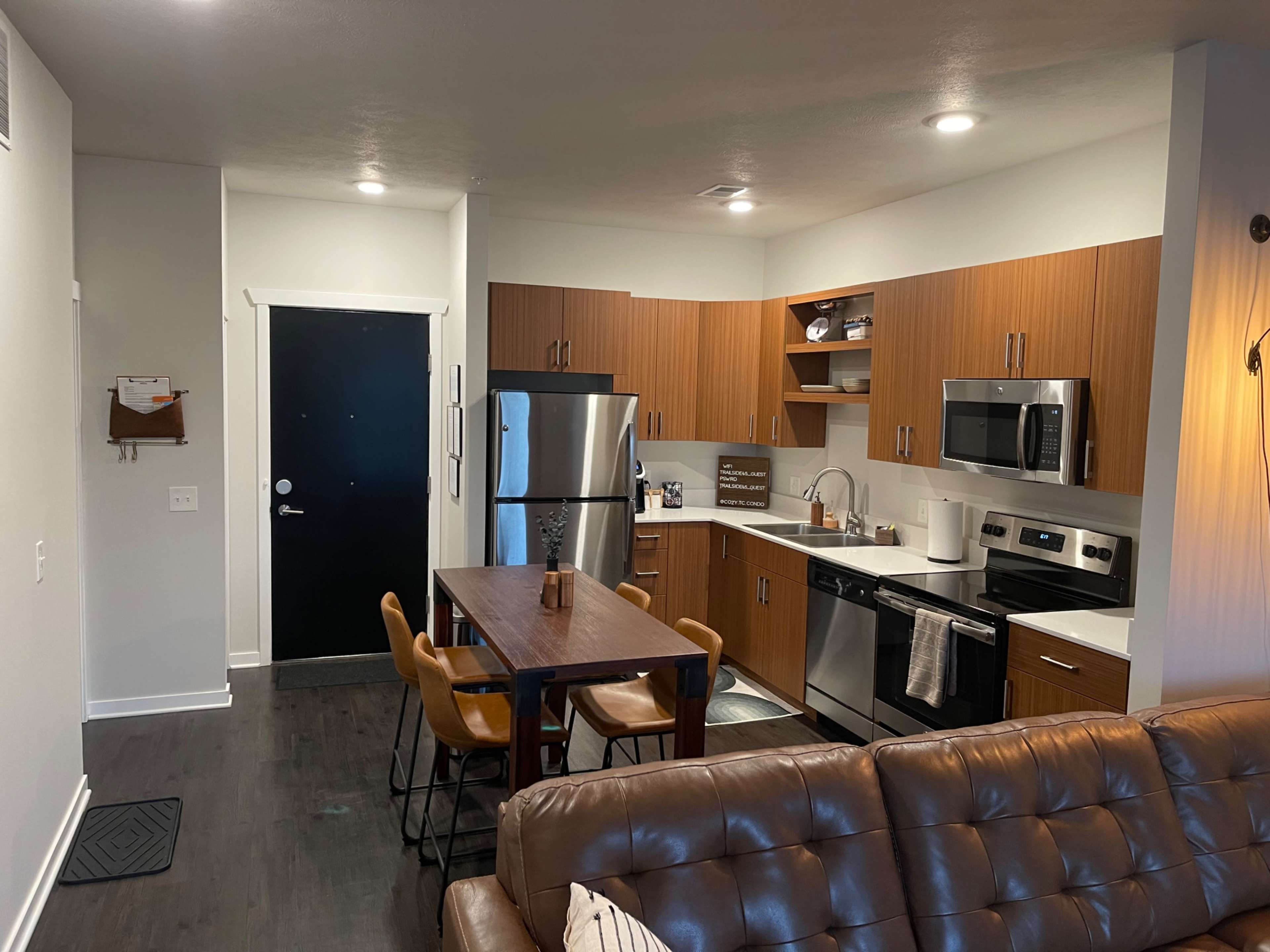 A modern kitchen and dining area with brown cabinets, stainless steel appliances, a wooden table, and leather seating.