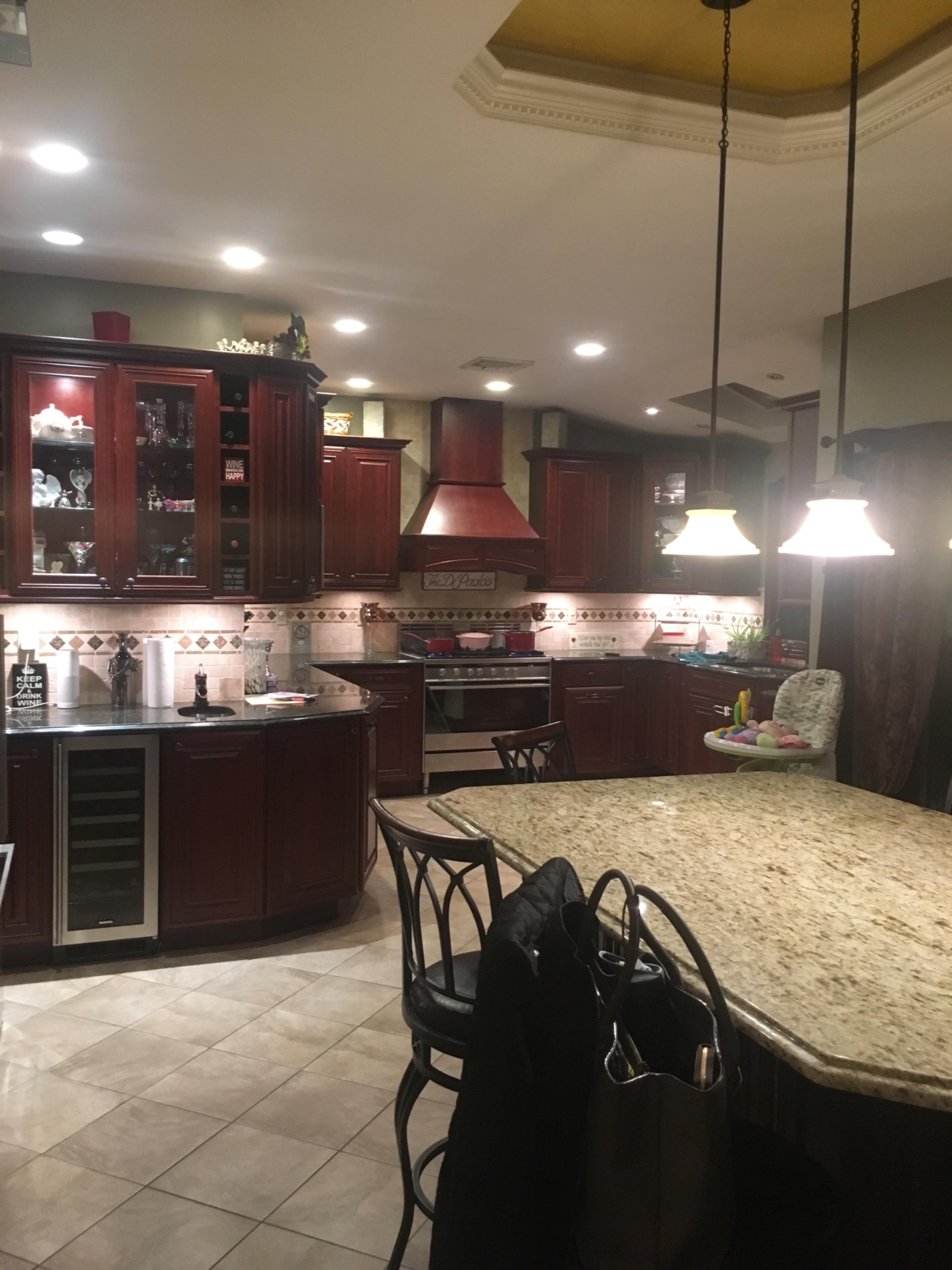 A spacious kitchen features dark wooden cabinetry, granite countertops, and an island with bar stools, illuminated by pendant lights.