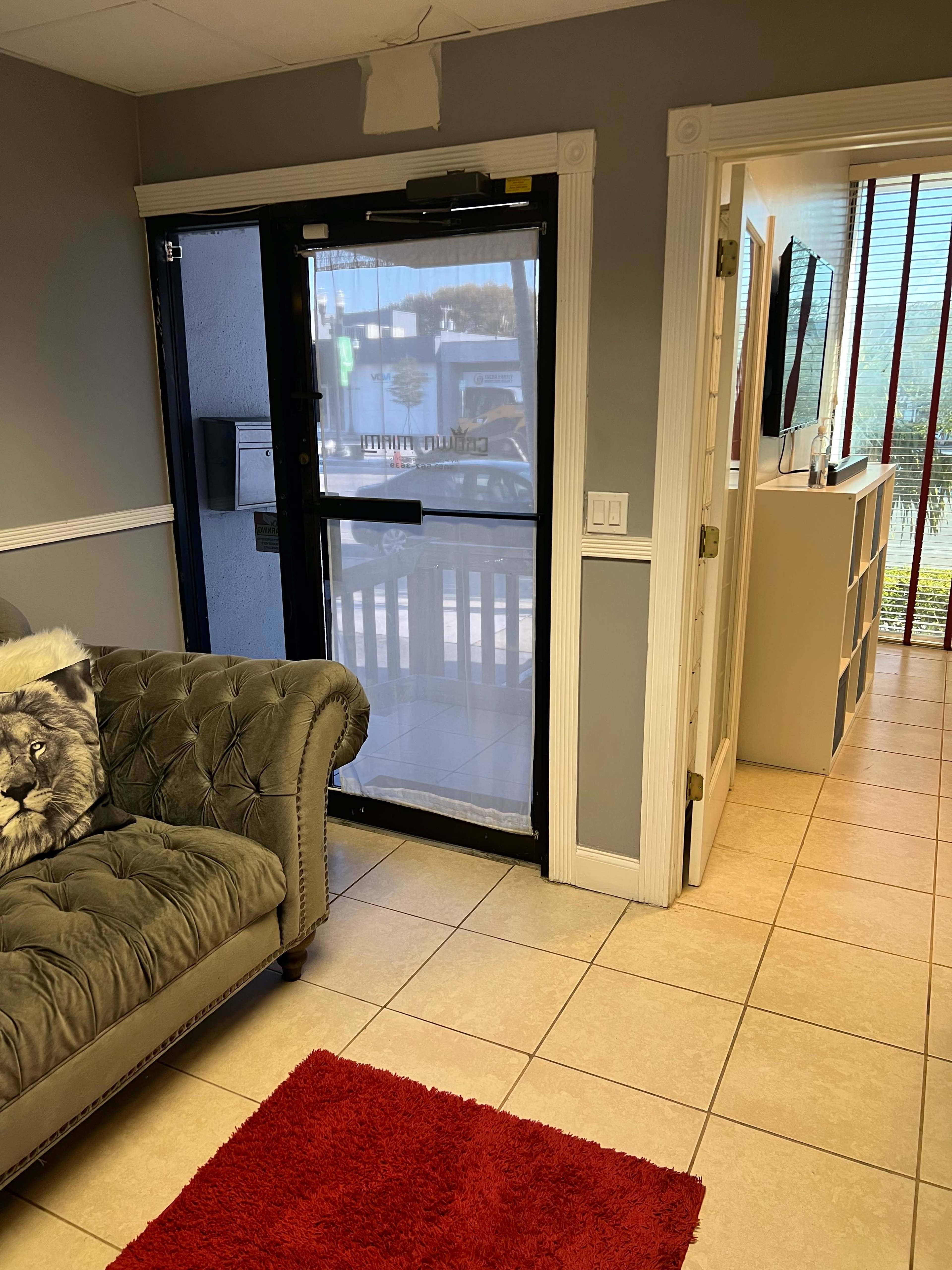 The image shows a lobby area with a green couch, a red rug, and a glass door leading outside.