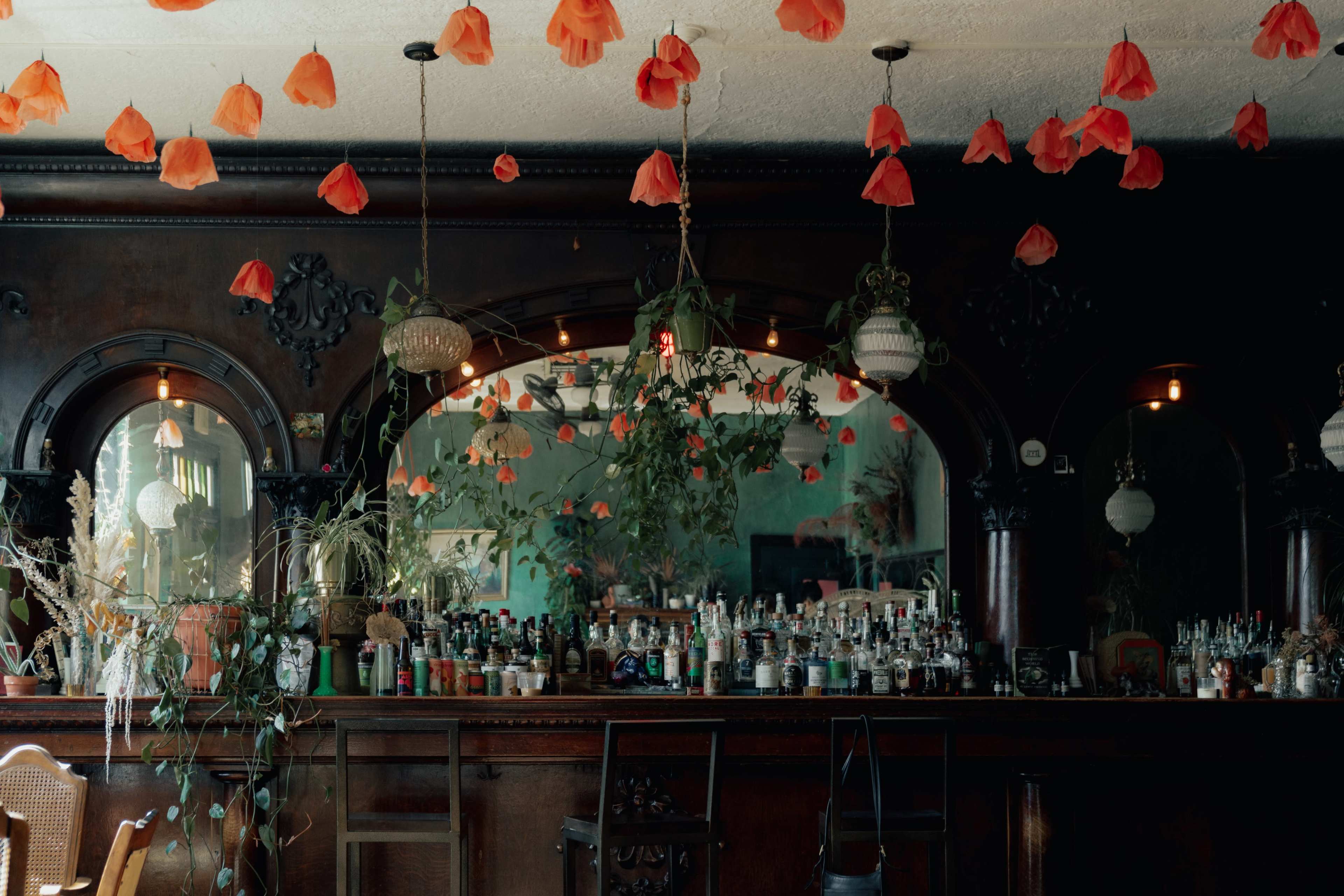 A bar interior decorated with hanging red flower petals and surrounded by dark wooden elements and plants.