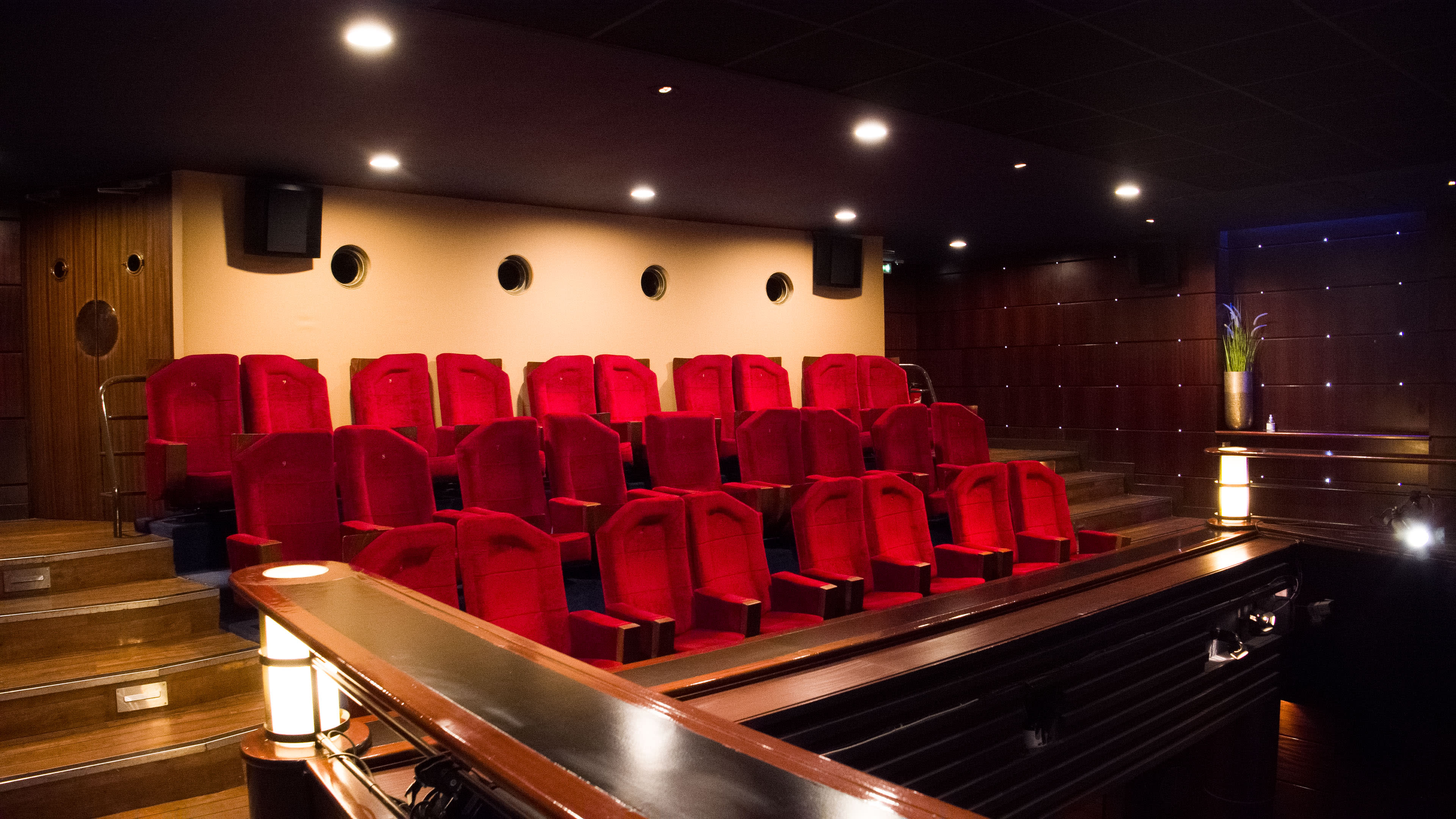A small, modern theater with red velvet seats arranged in a tiered layout.