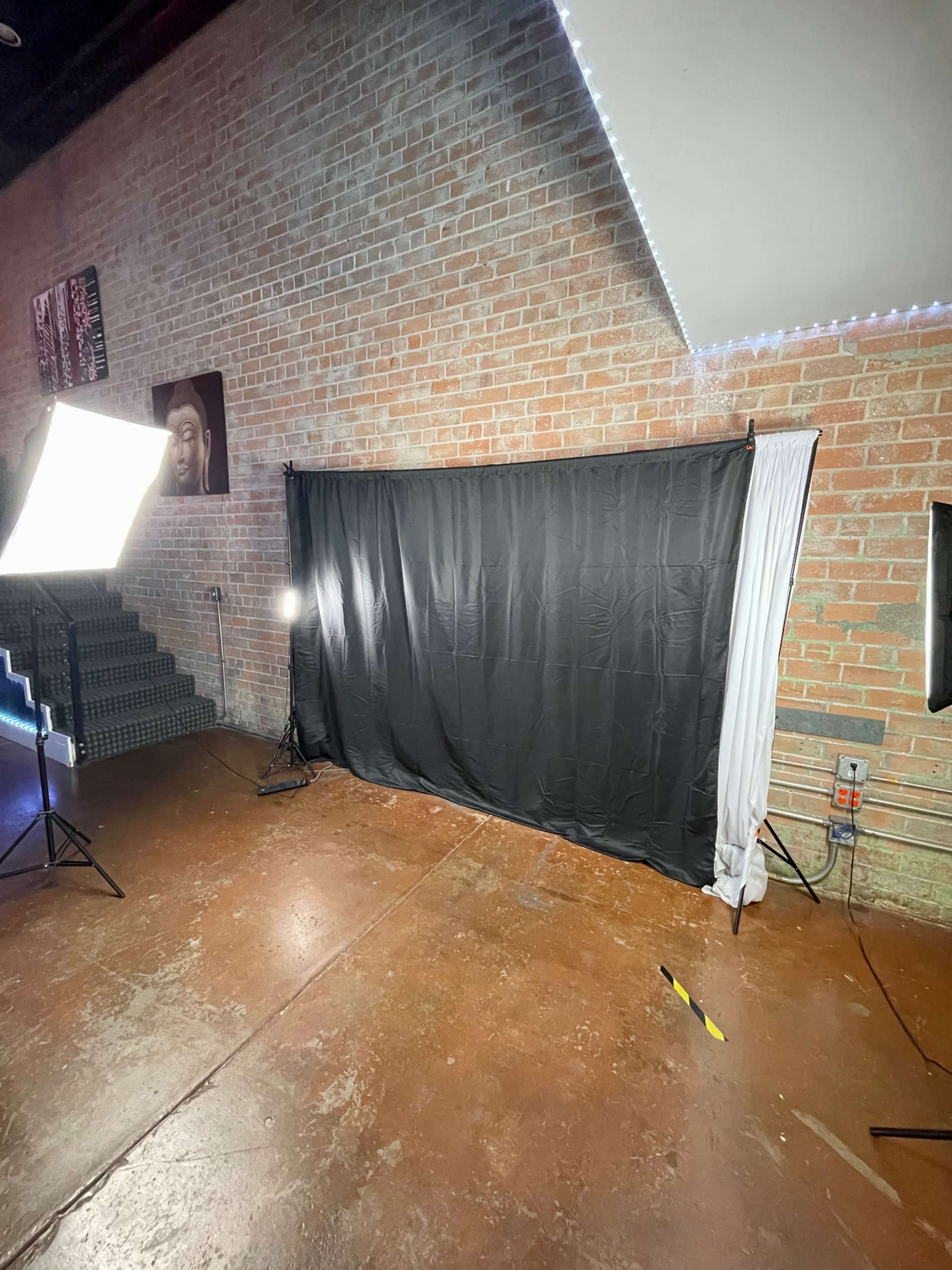 A photography setup with a black backdrop, softbox lights, and a white drape in front of a brick wall.
