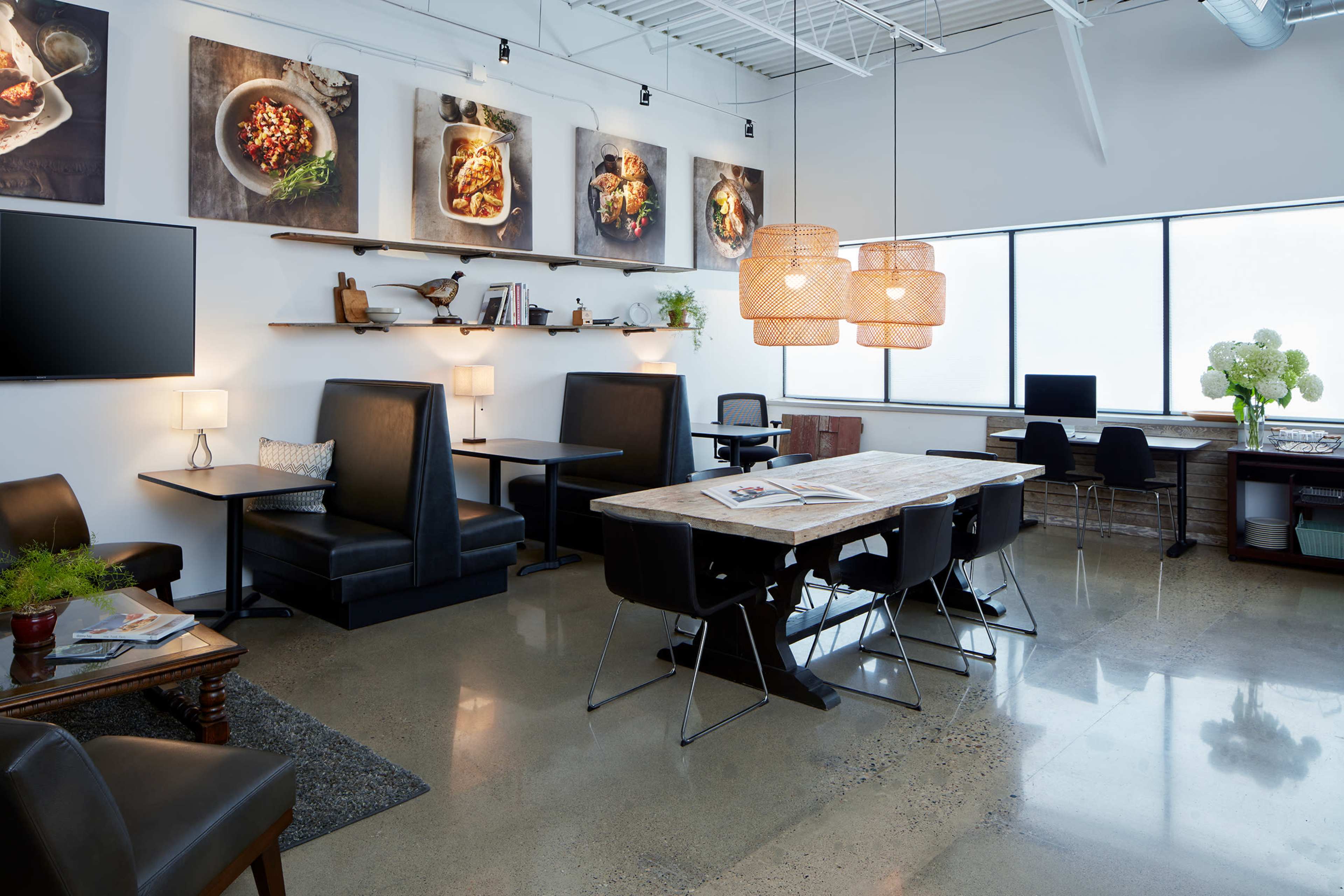 A modern office space with various seating areas, a large wooden table, and wall-mounted artworks.