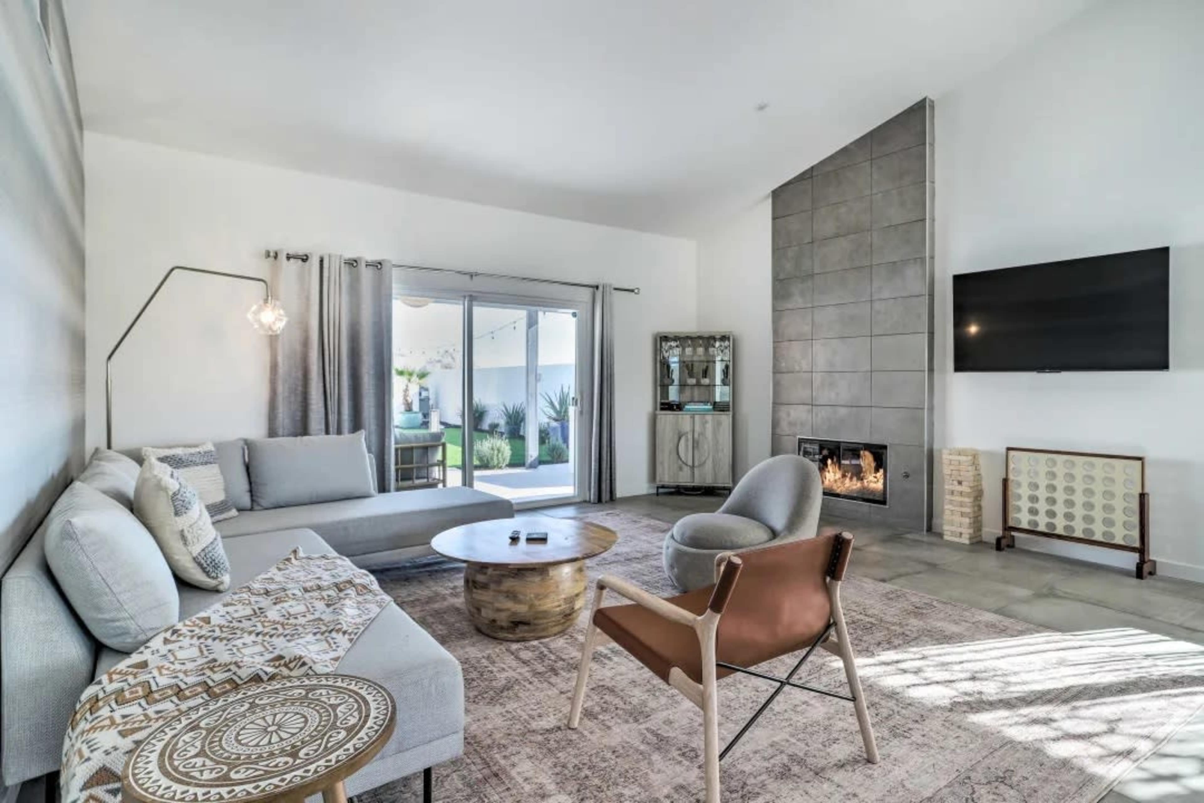 The image shows a modern living room with a fireplace, a circular coffee table, and a combination of gray and beige furniture.