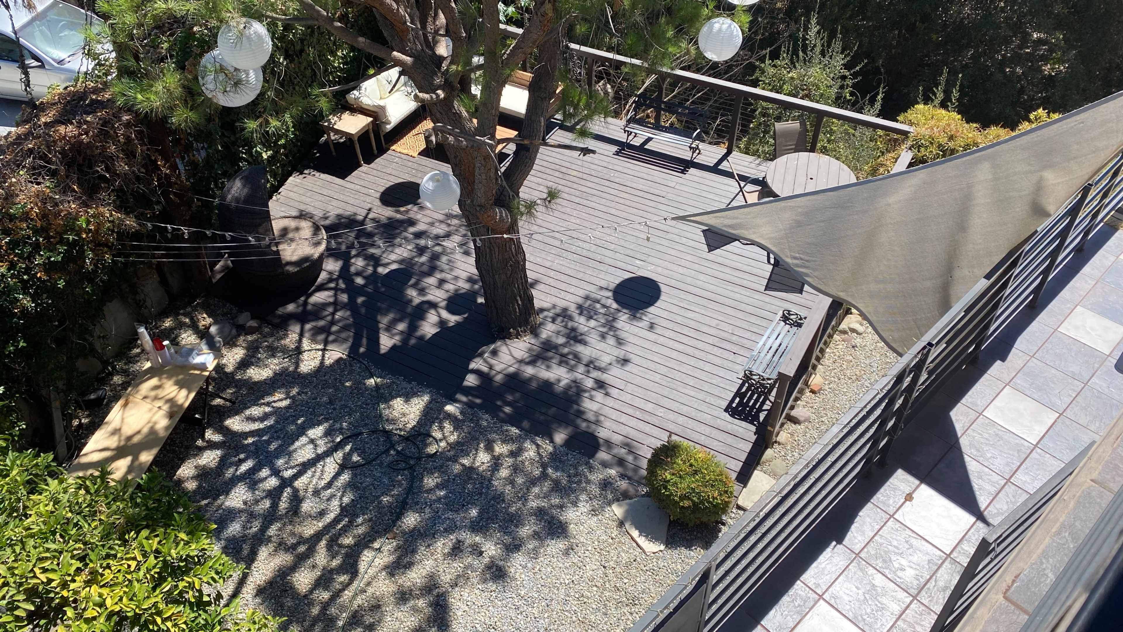 A wooden deck featuring round tables and outdoor seating surrounded by greenery and decorative lights.