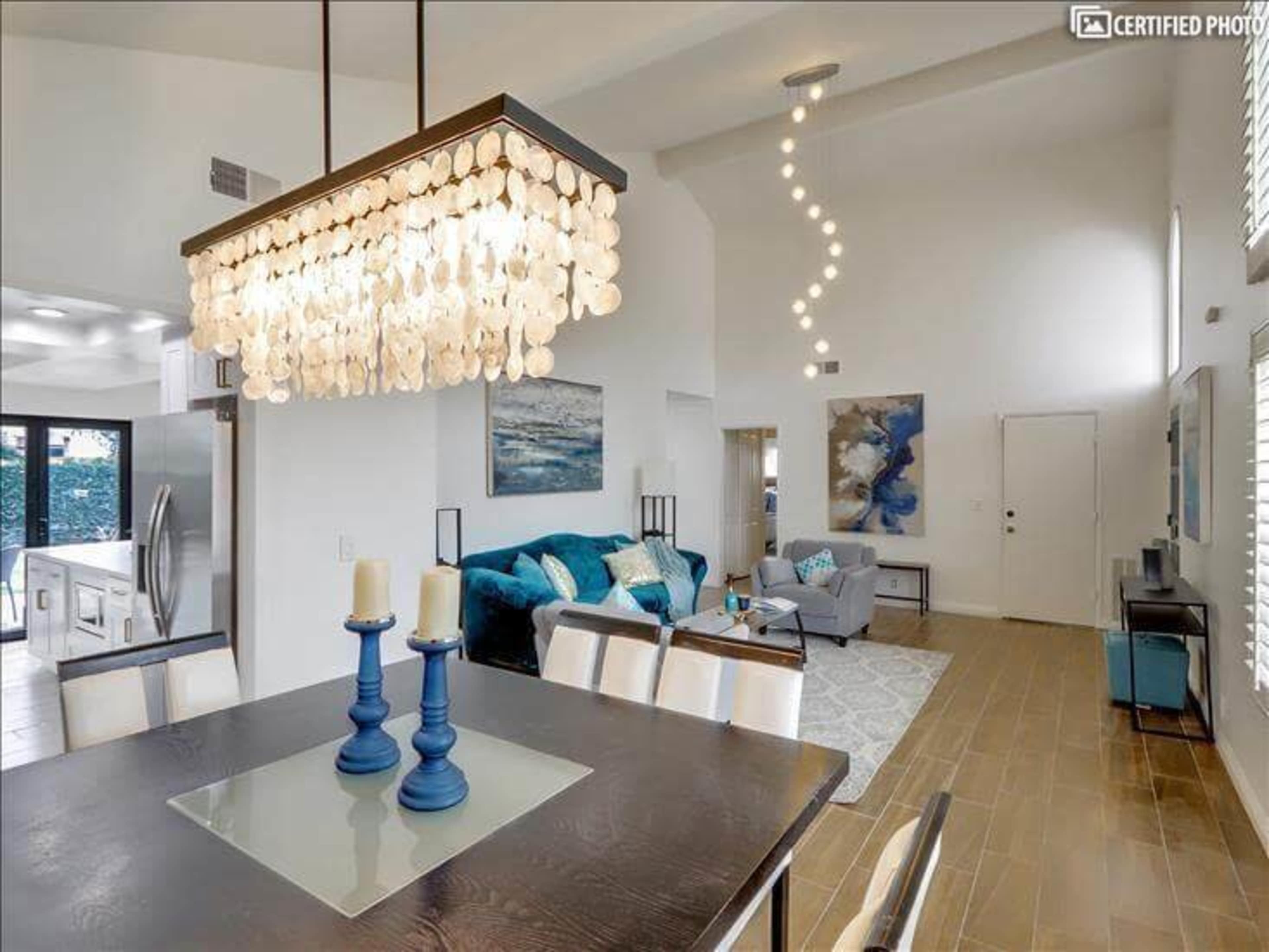 A modern living space with a dining area featuring a large chandelier, a cozy seating arrangement, and bright natural light.