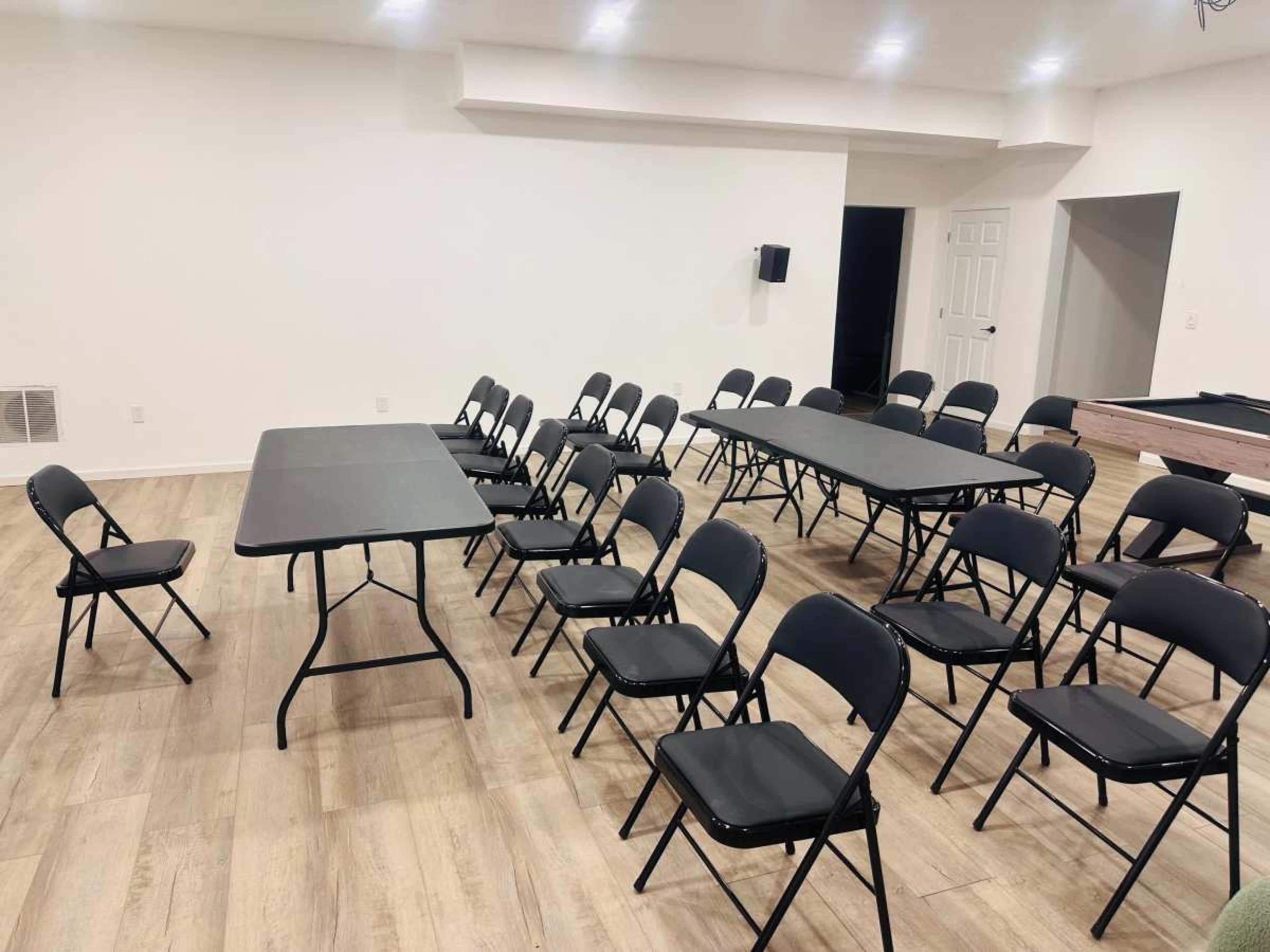 The image shows a room with several black folding chairs arranged around multiple tables, featuring a pool table in the corner.