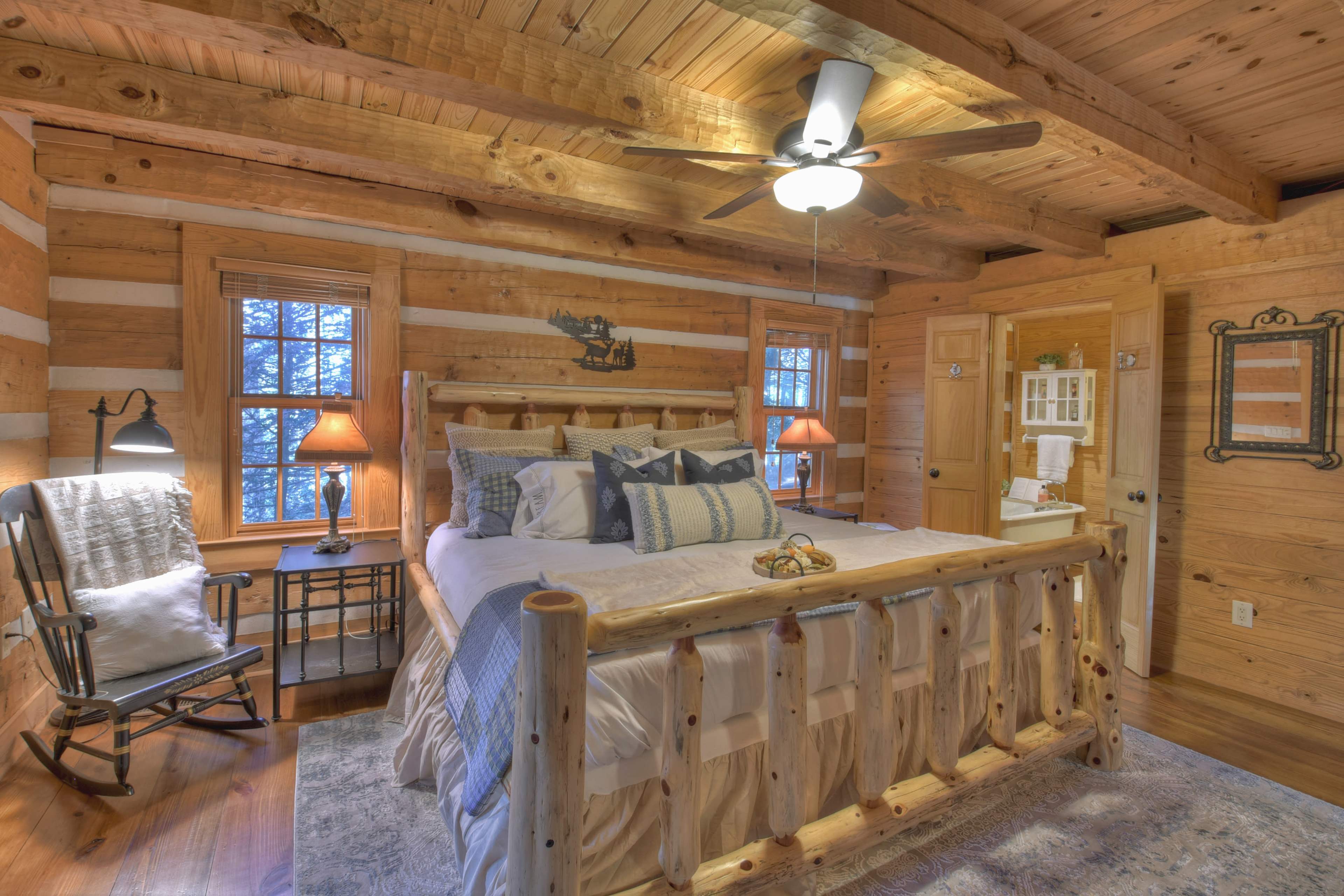 A rustic wooden bedroom featuring a log-style bed, a rocking chair, and warm lighting from bedside lamps.