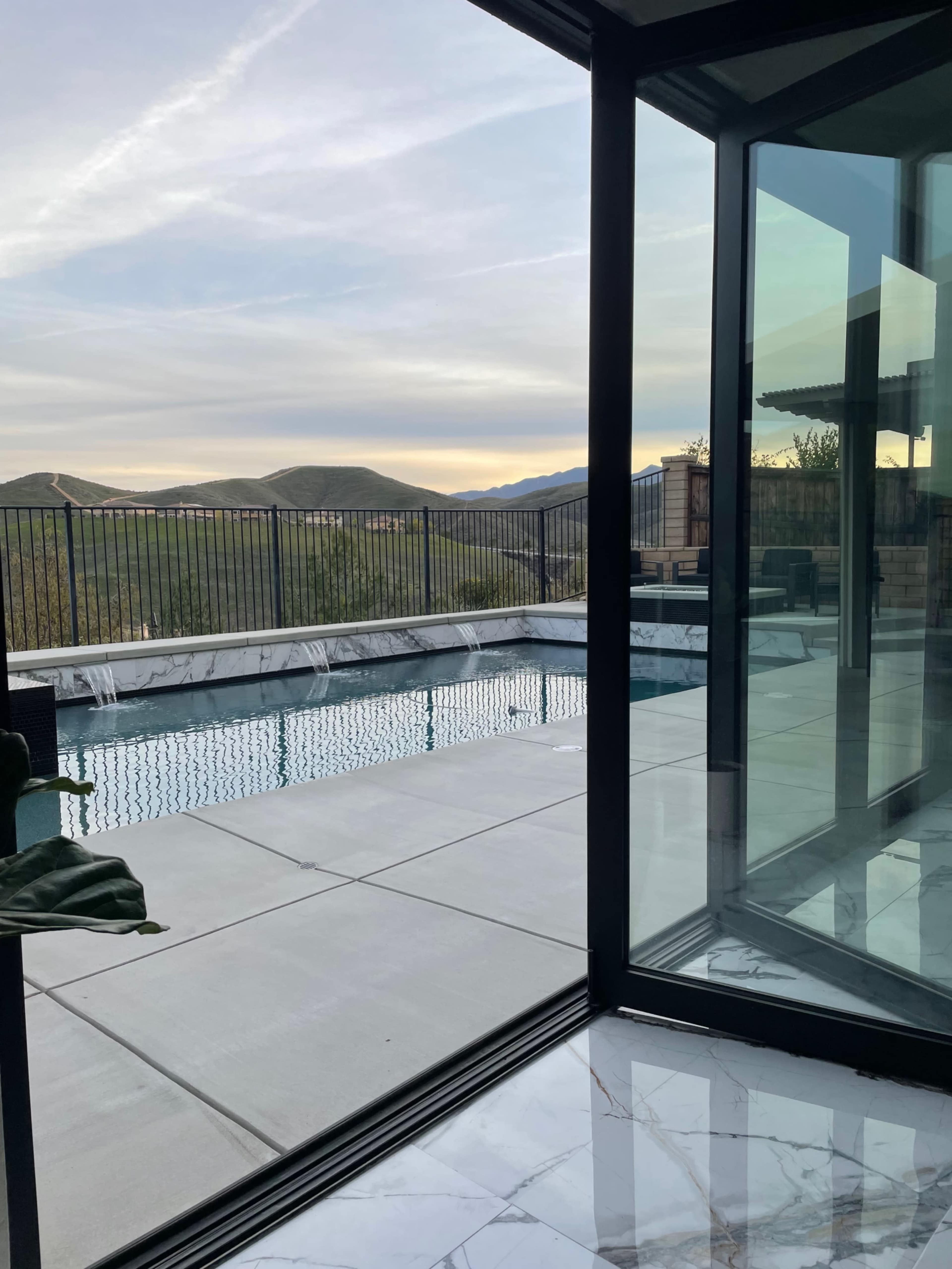 A modern indoor space with floor-to-ceiling glass walls overlooking a swimming pool and mountainous landscape.