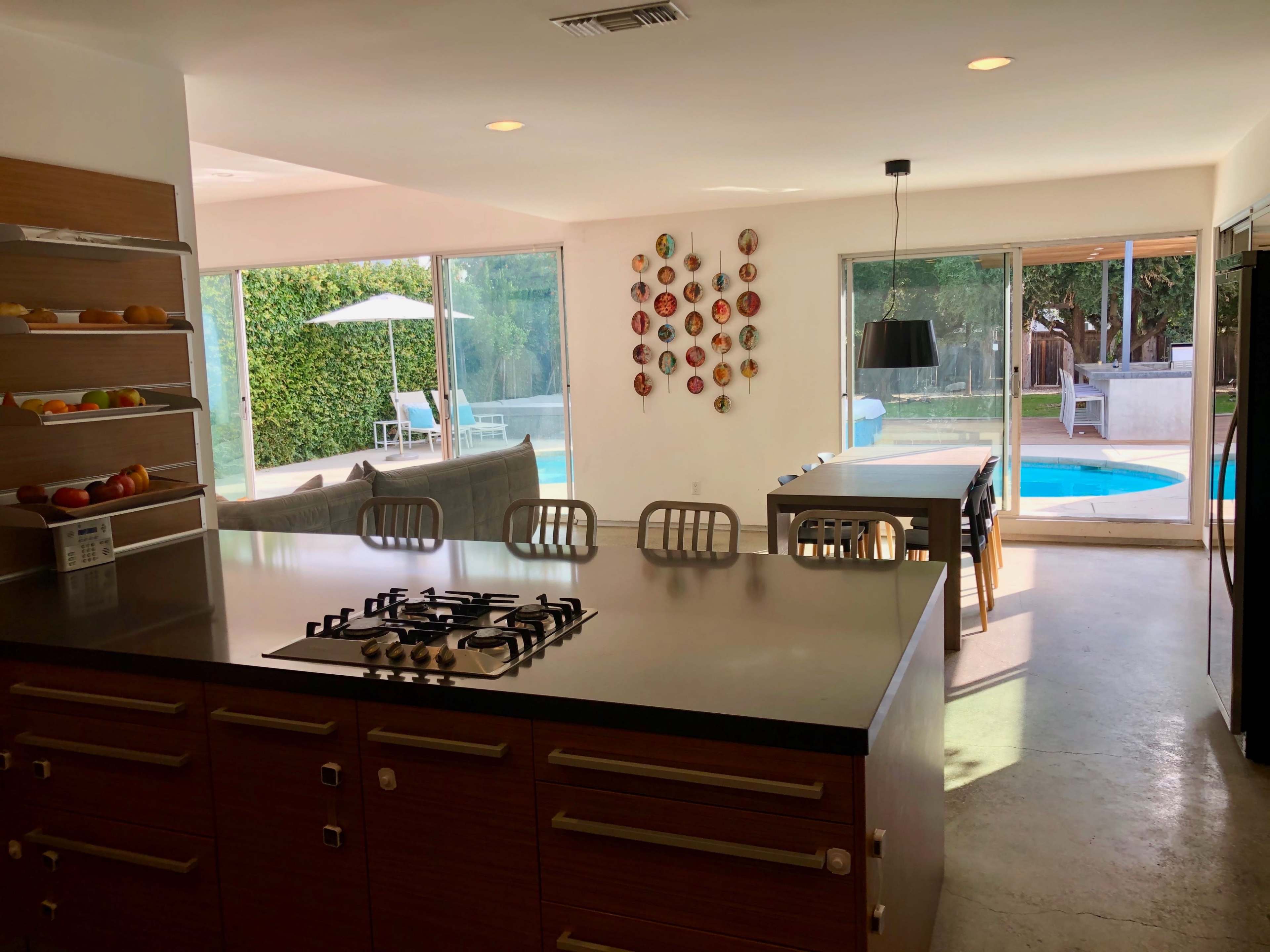 A modern kitchen with a gas stove overlooks an outdoor pool area through large glass doors.