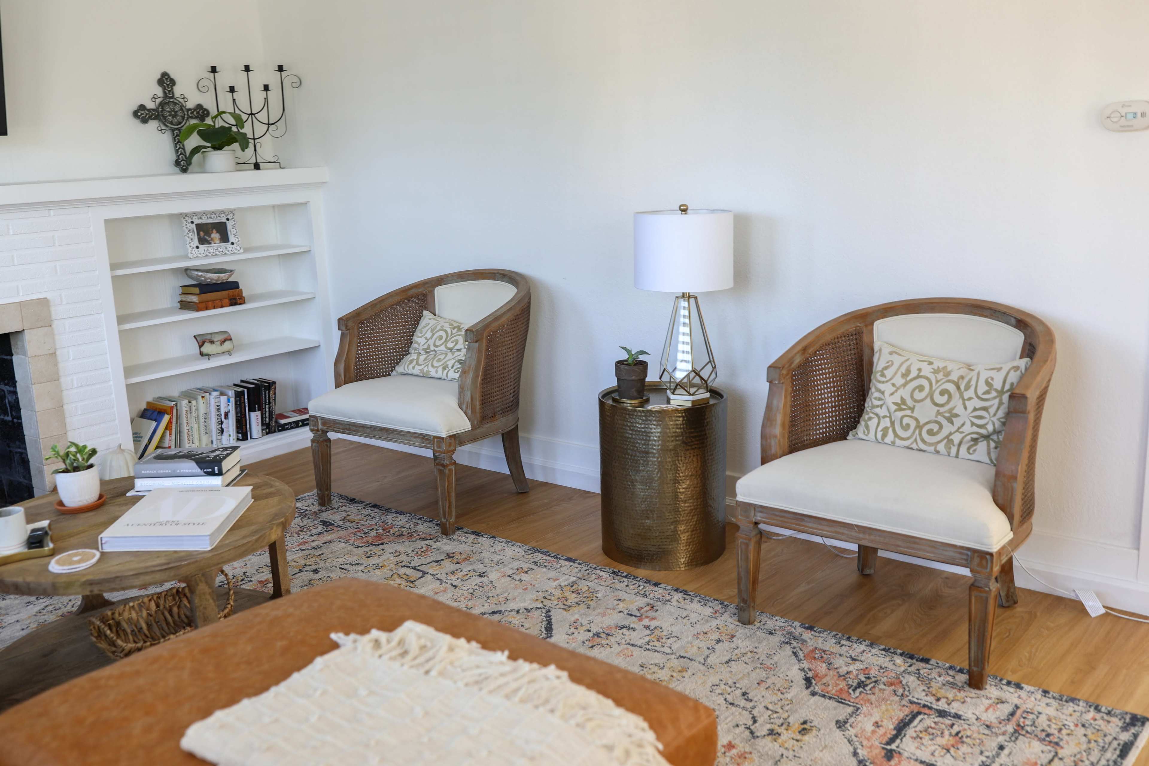 A cozy living room with two wicker armchairs, a small round table, and a bookshelf filled with books.