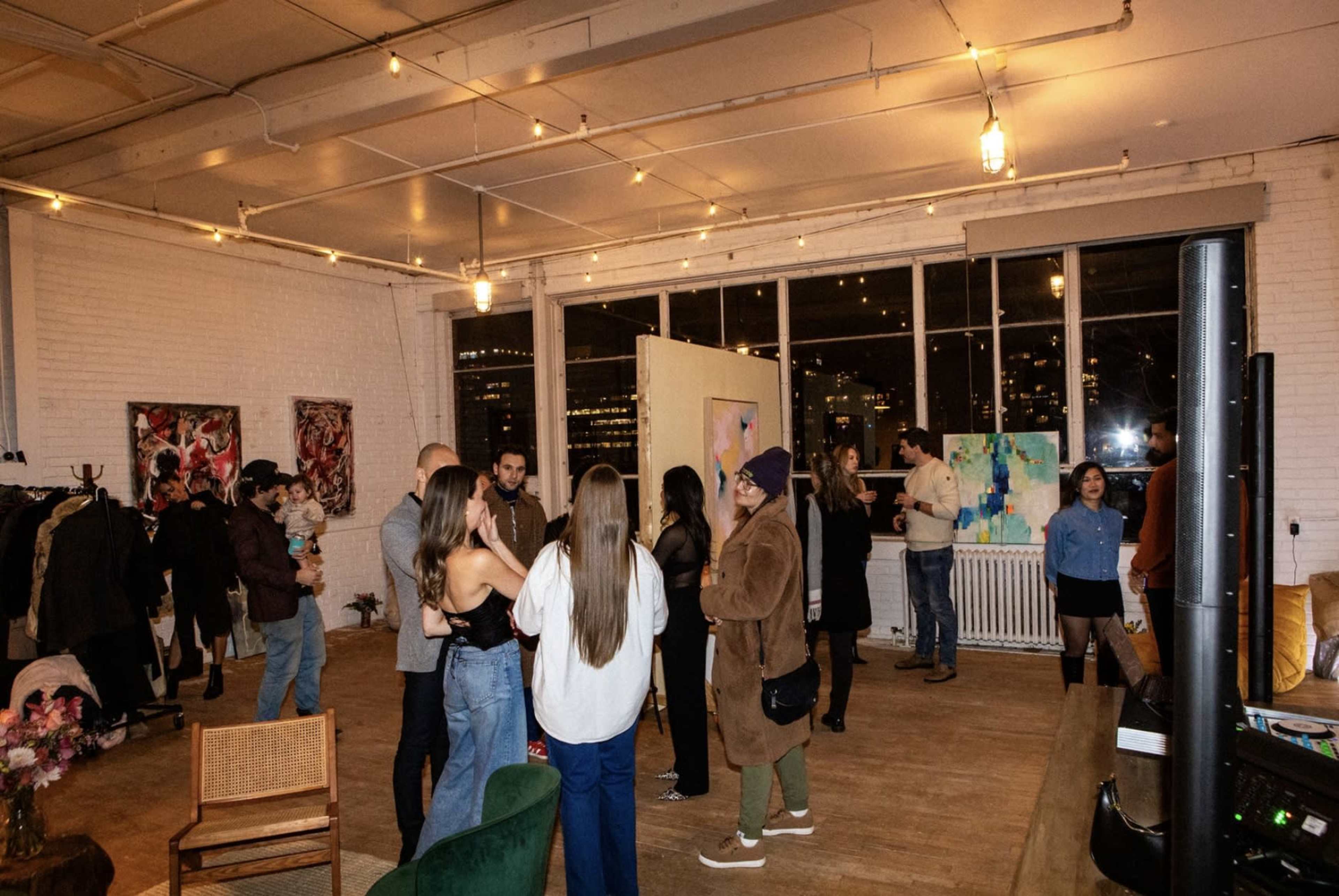 A group of people socialize in an art gallery featuring various paintings and twinkling lights.