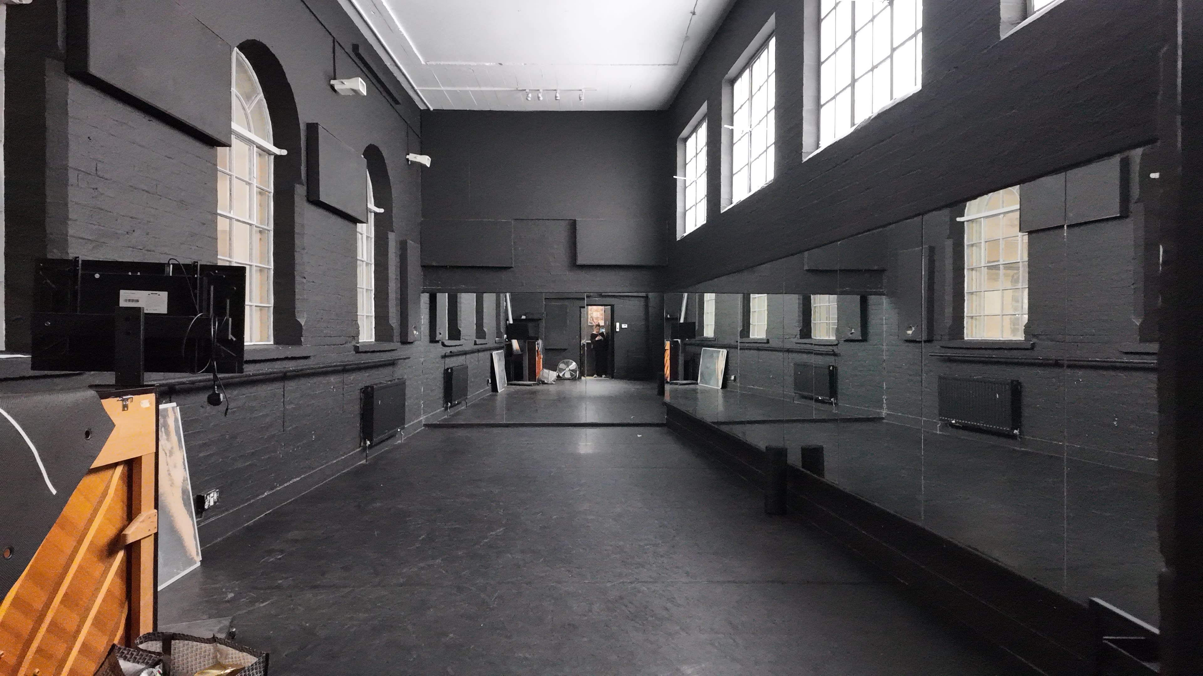 The image shows a long, narrow dance studio with black walls and large mirrors lining one side.