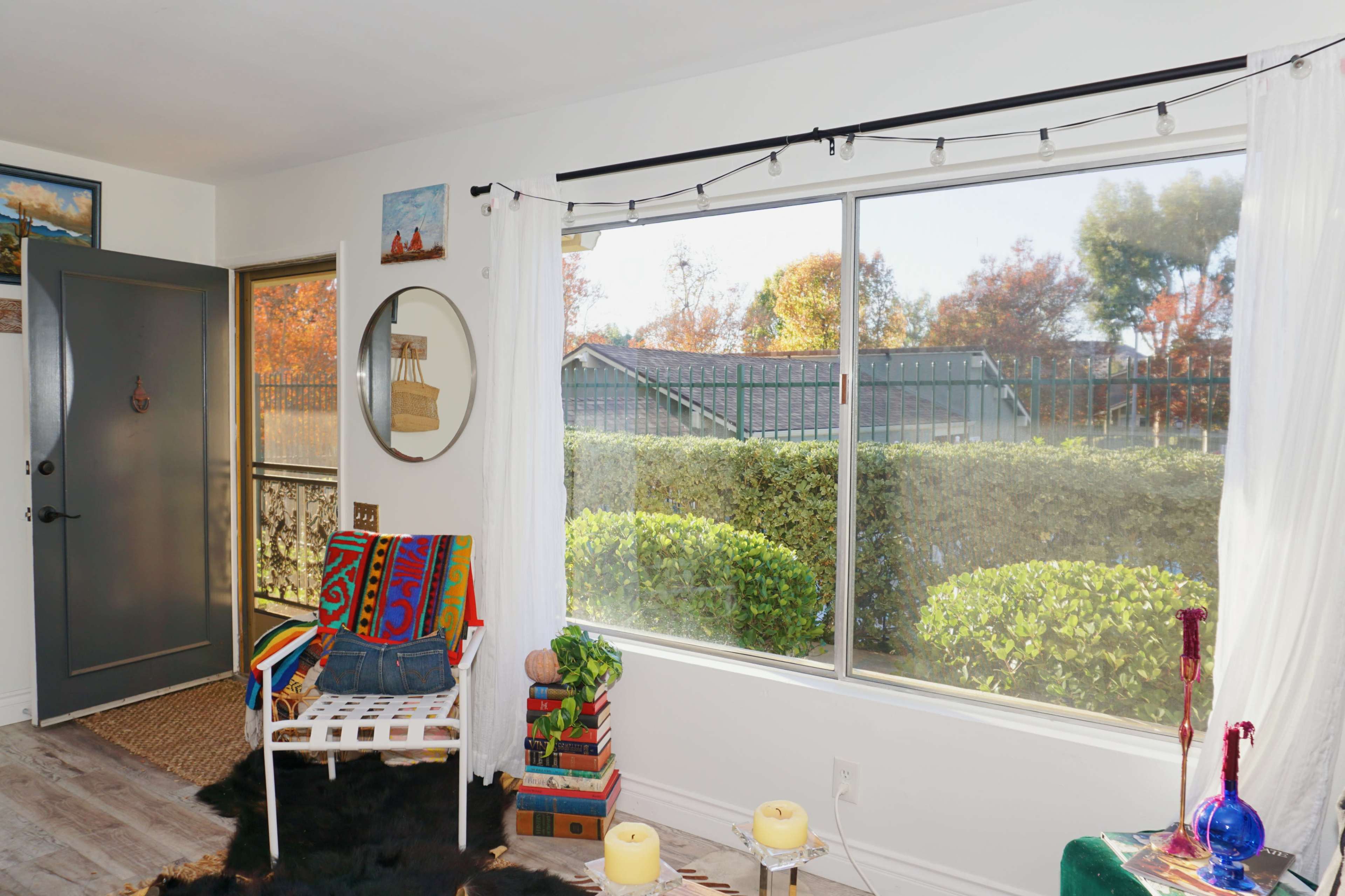 A brightly lit living area with a large window overlooking a landscaped garden, featuring colorful decor and a comfortable chair.
