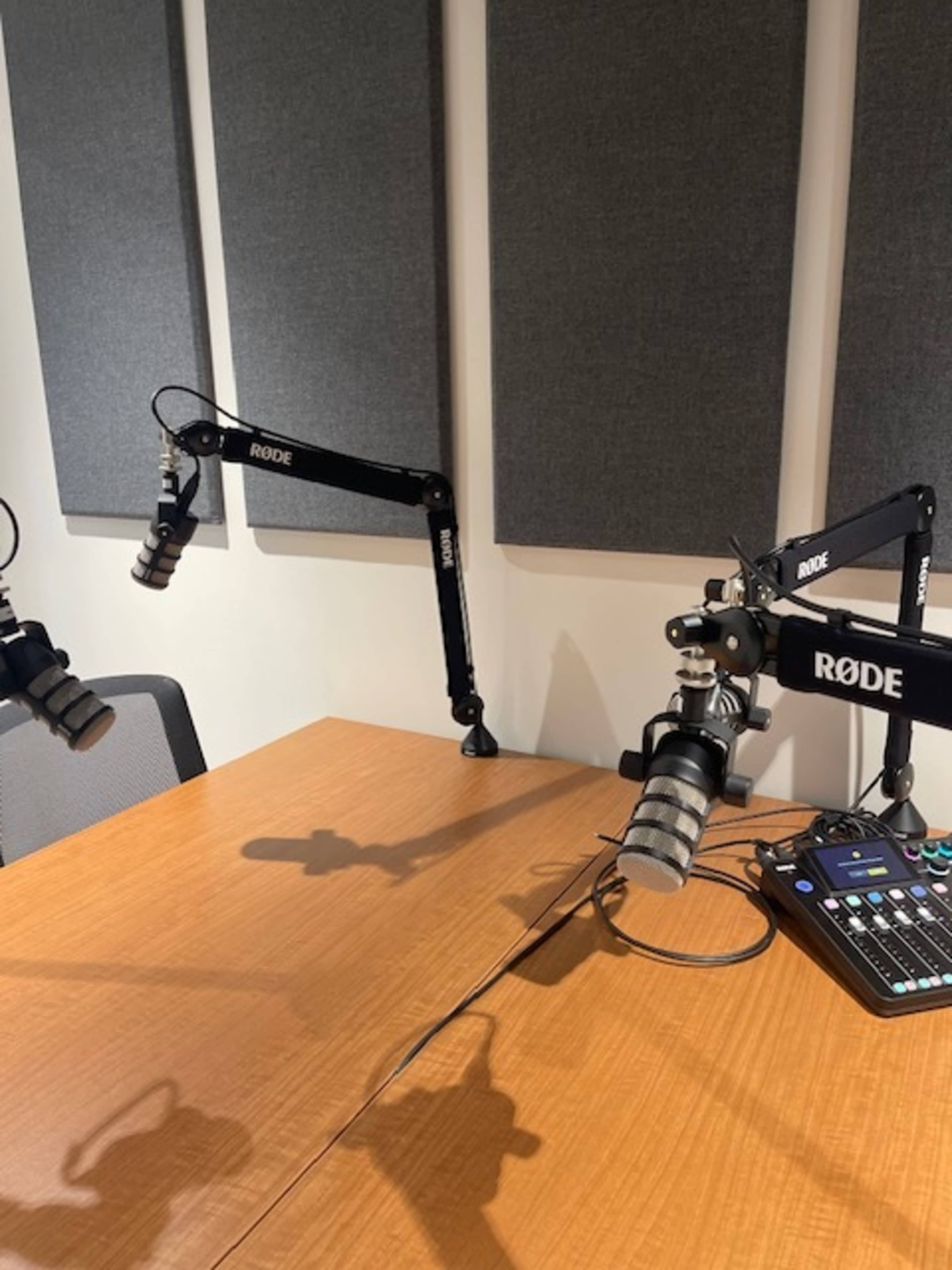 A radio studio setup featuring two microphone stands, a wooden table, and an audio mixer on the surface.
