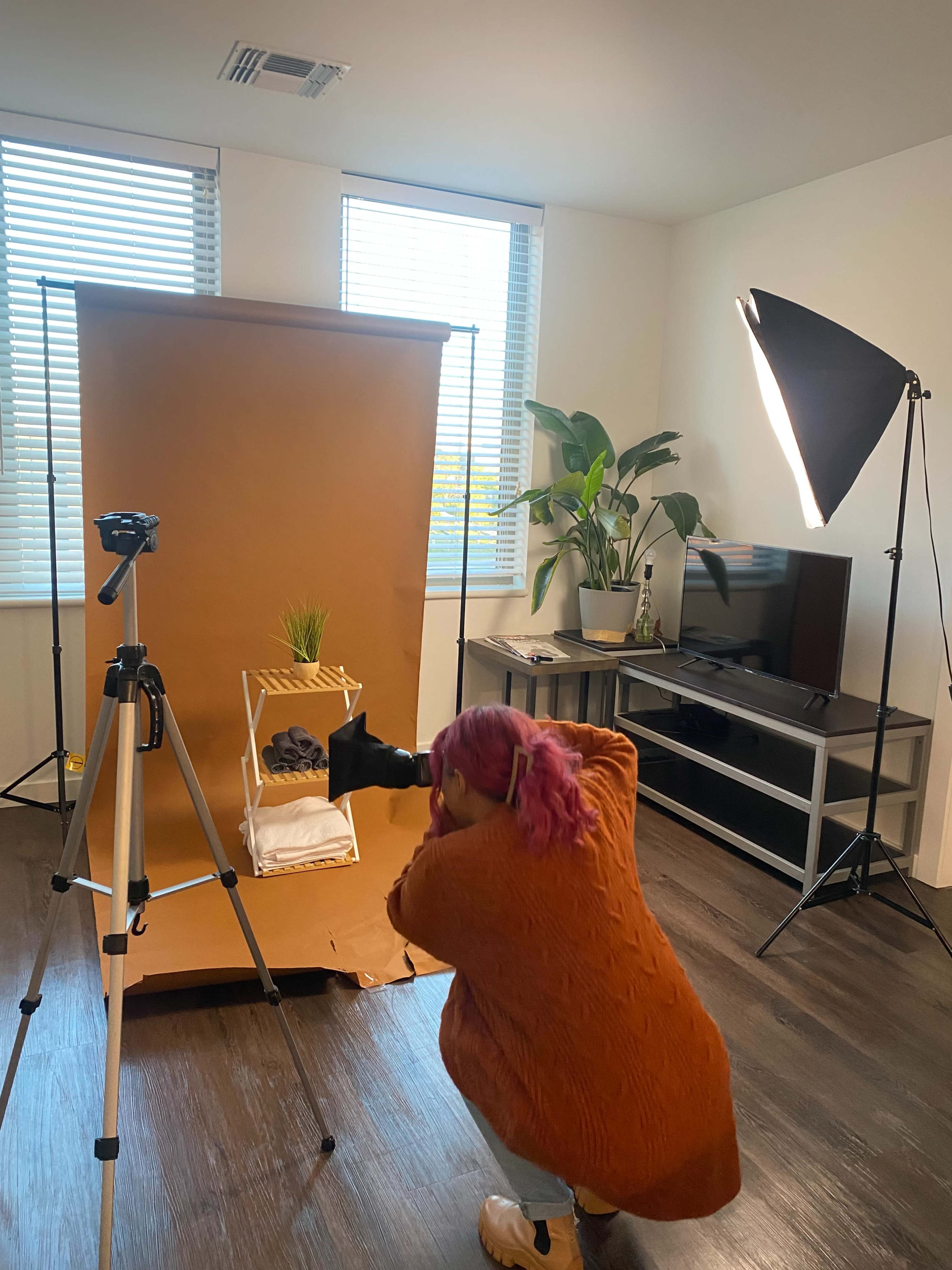 A person is taking a photo of a small display setup featuring a plant and folded towels in a well-lit room.