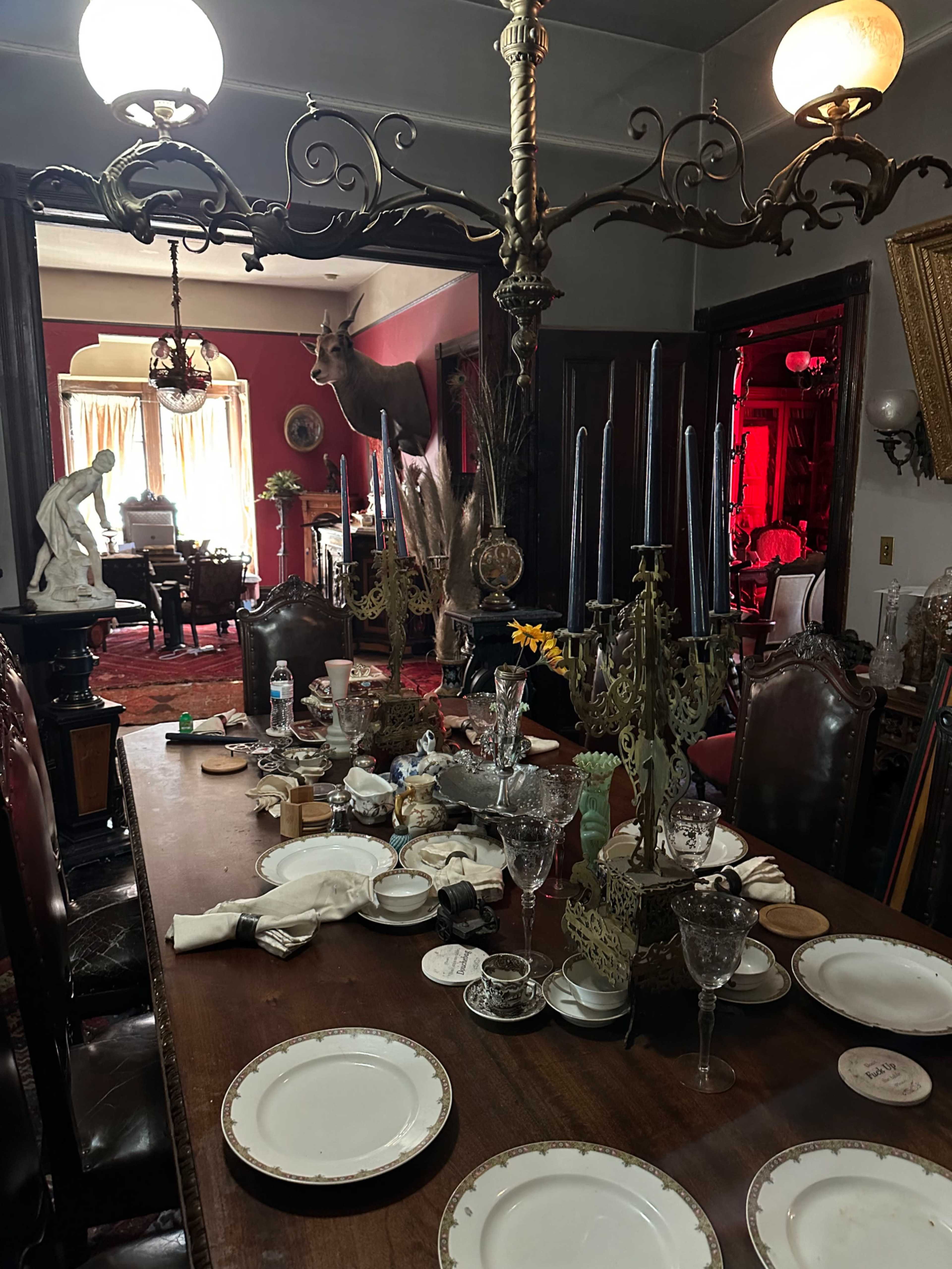 A dining room table set with various dishes and glassware, while a deer head mounted on the wall overlooks the scene.