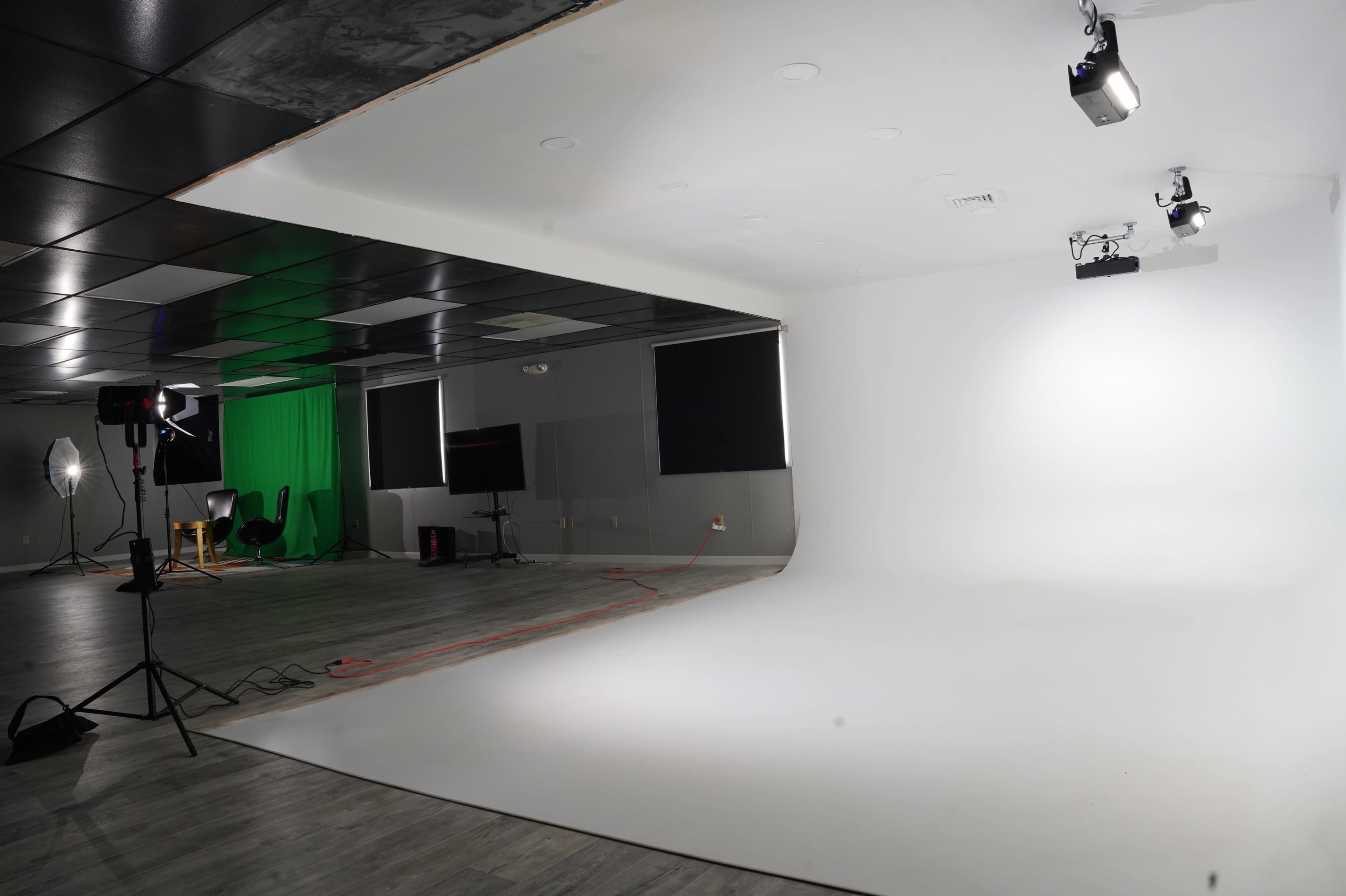 A photography studio features a white seamless backdrop and a green screen, with various lighting equipment set up around the space.